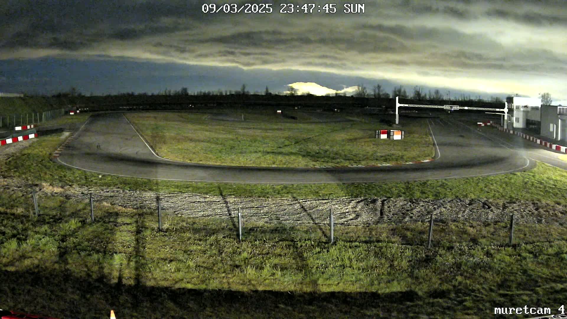 An empty go-kart track at night under a cloudy sky.