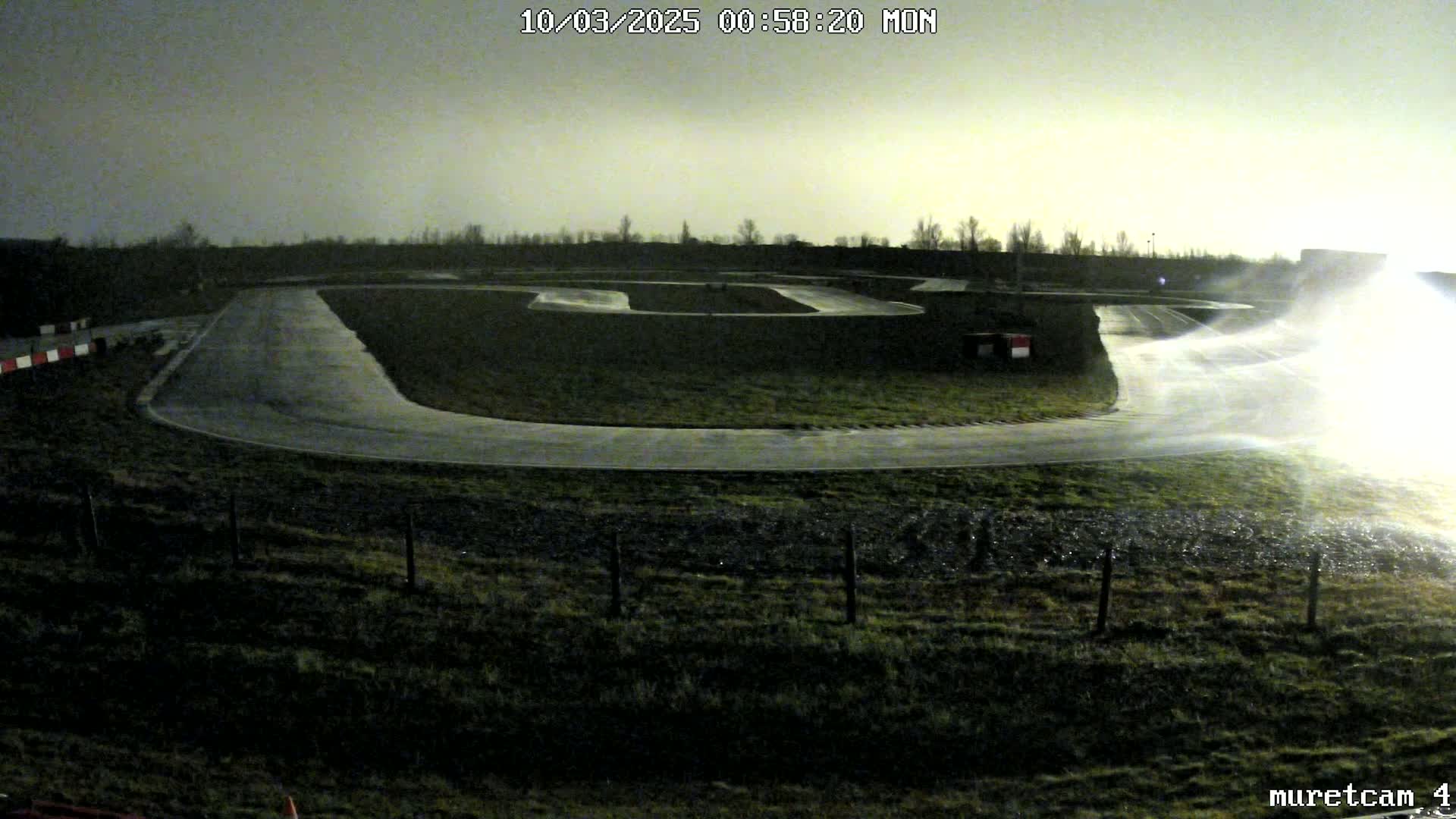 A wet go-kart track is visible at night under a dim, overcast sky.