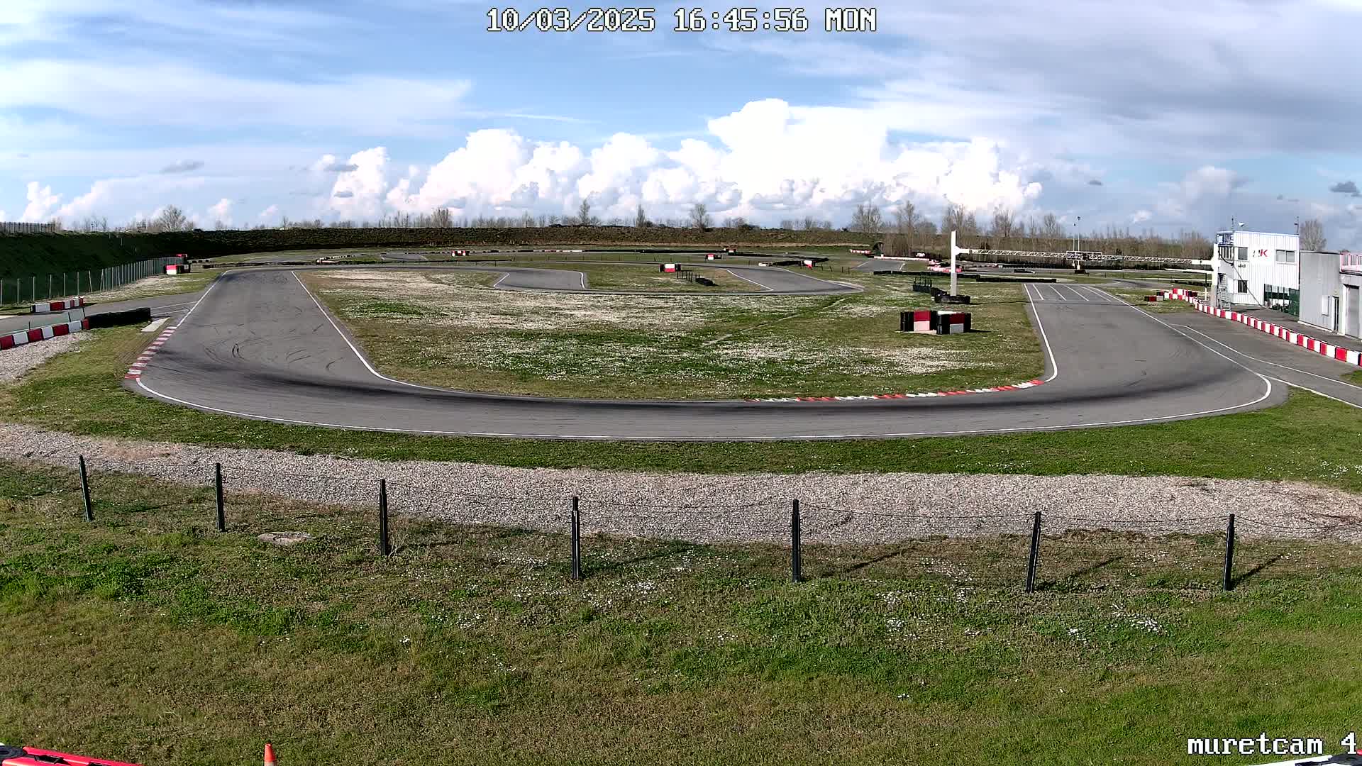 An empty asphalt go-kart track with a grassy center and surrounding area under a partly cloudy sky.