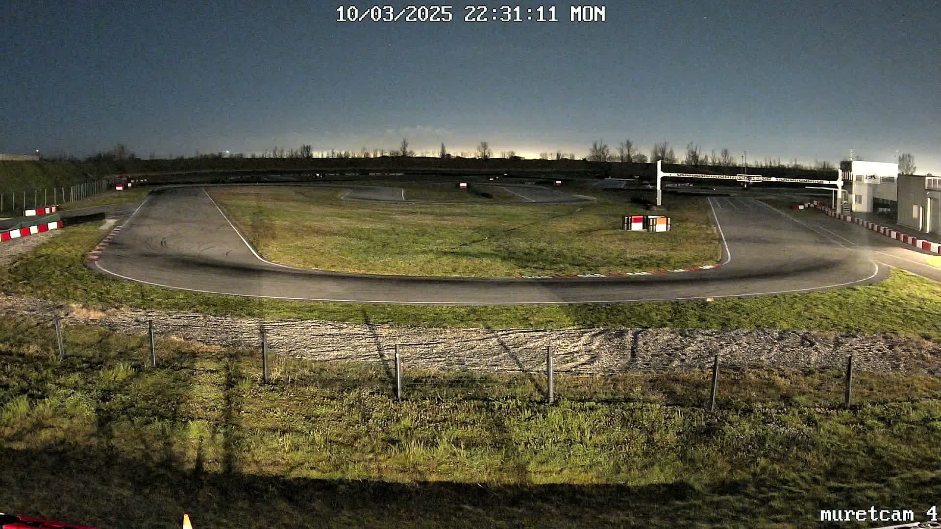 An empty asphalt go-kart track is visible at night under a clear, dark sky.