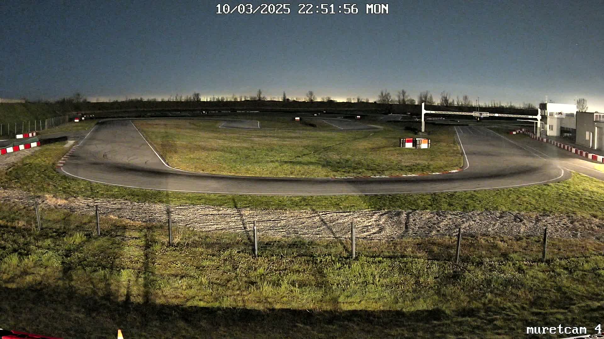 An empty go-kart track is illuminated at night under a twilight sky.