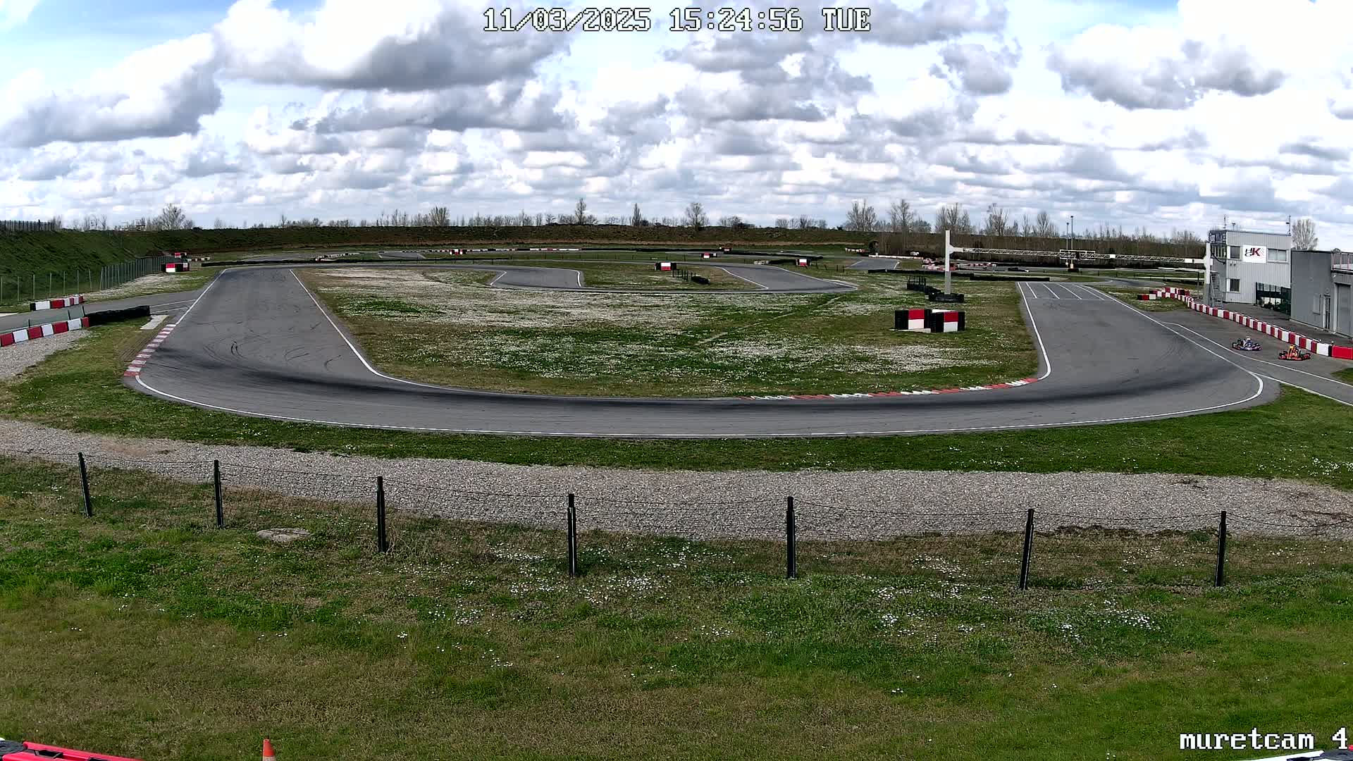 An outdoor go-kart track with a few karts visible under a partly cloudy sky.