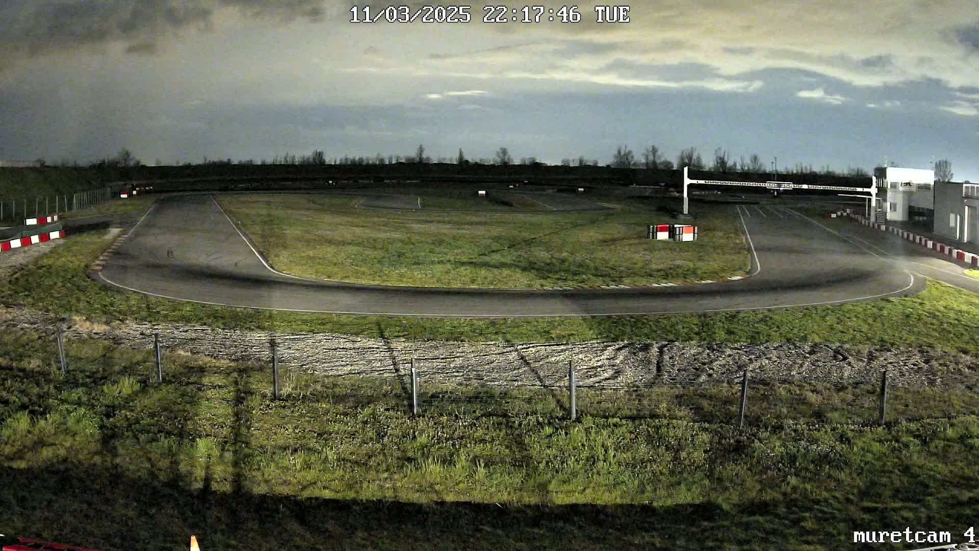A nighttime view of a paved go-kart track under a cloudy sky.