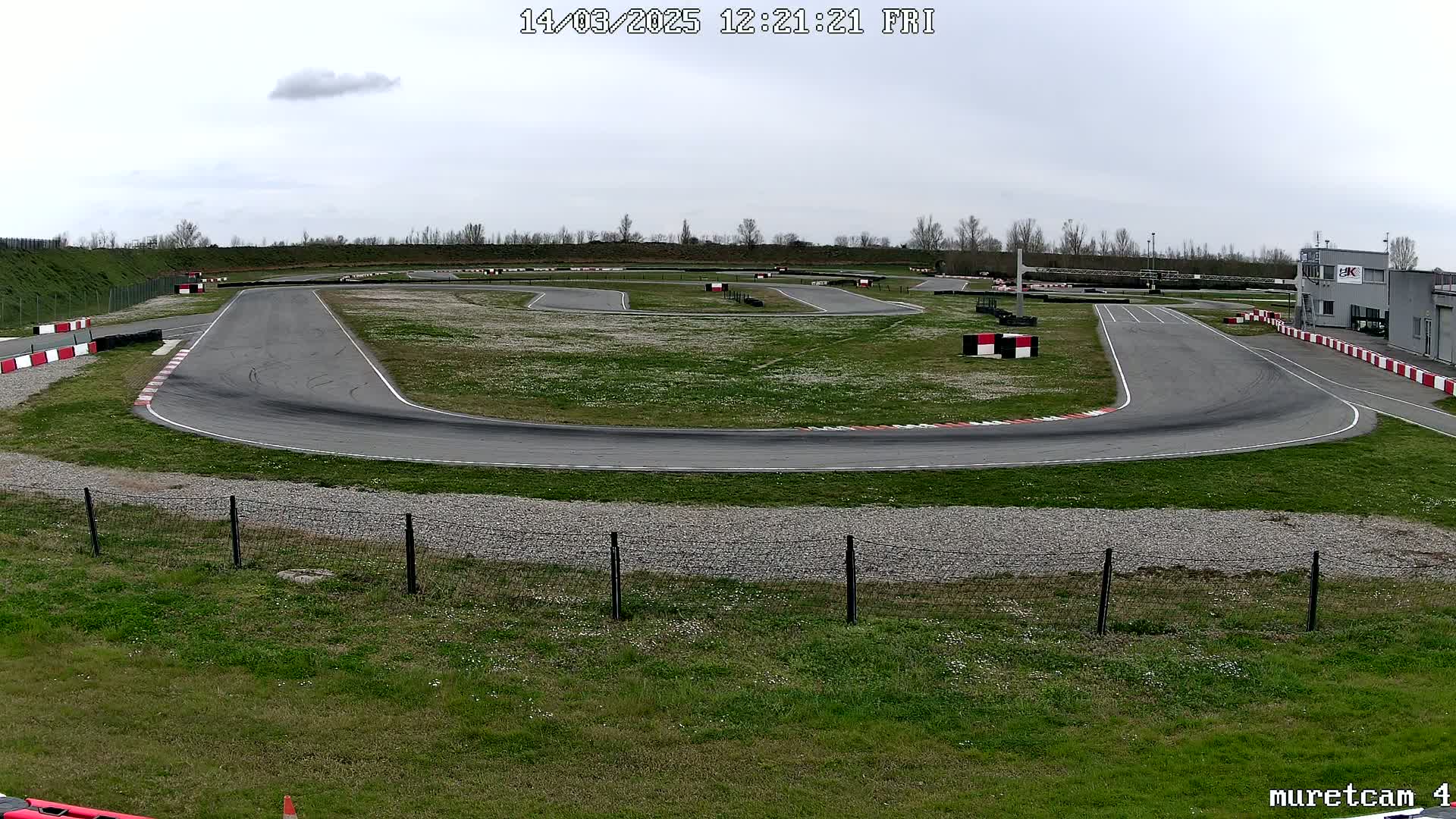 An outdoor go-kart track with a winding asphalt course surrounded by grass under an overcast sky.