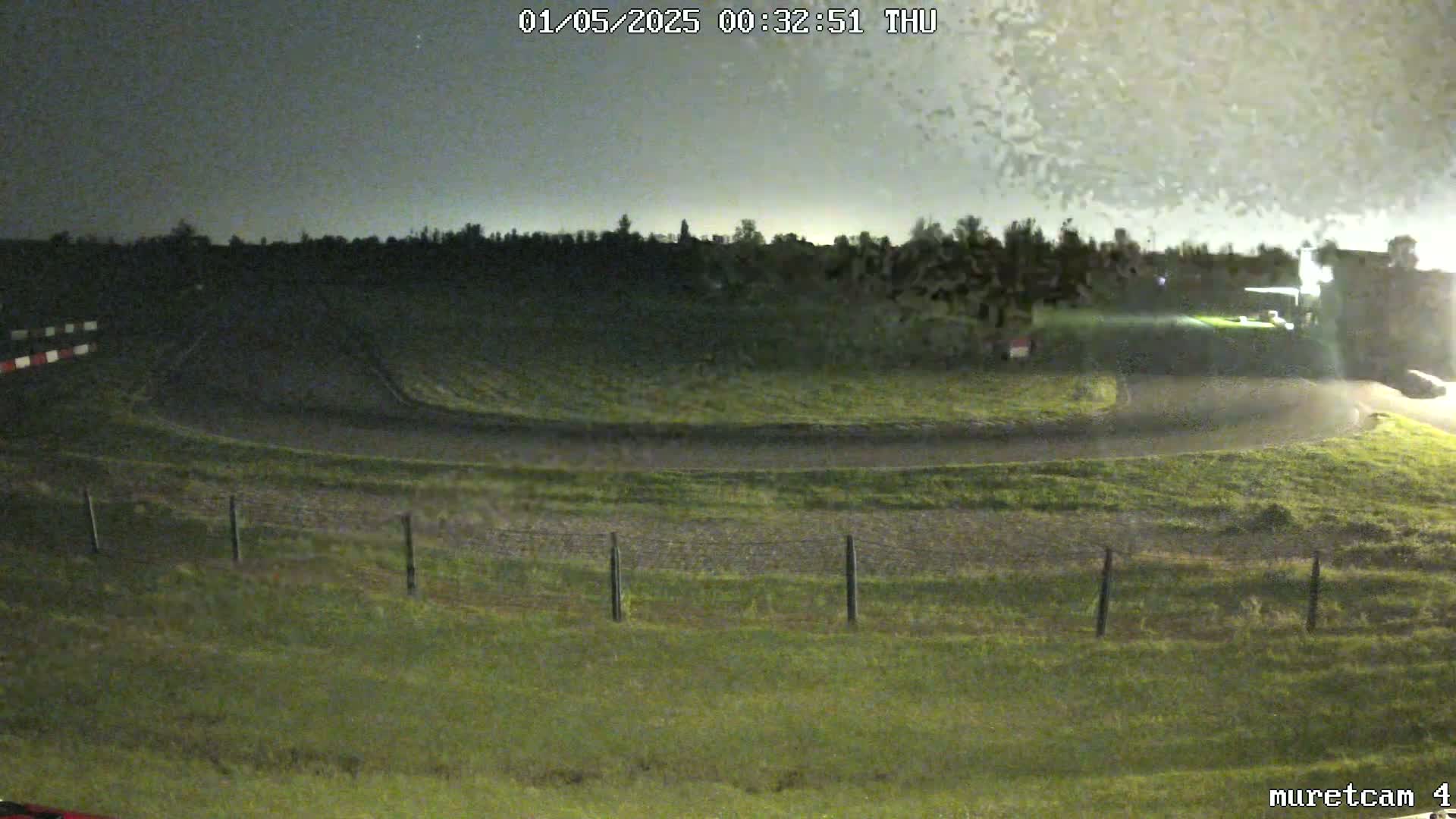 A nighttime view of a grassy area with a curved road and a fence under an overcast sky.