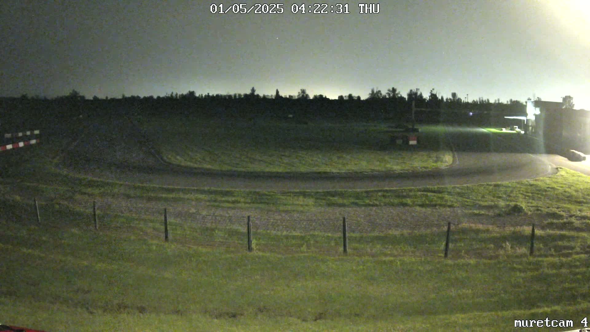 A dark, grassy area with a curved asphalt track under a nighttime sky.