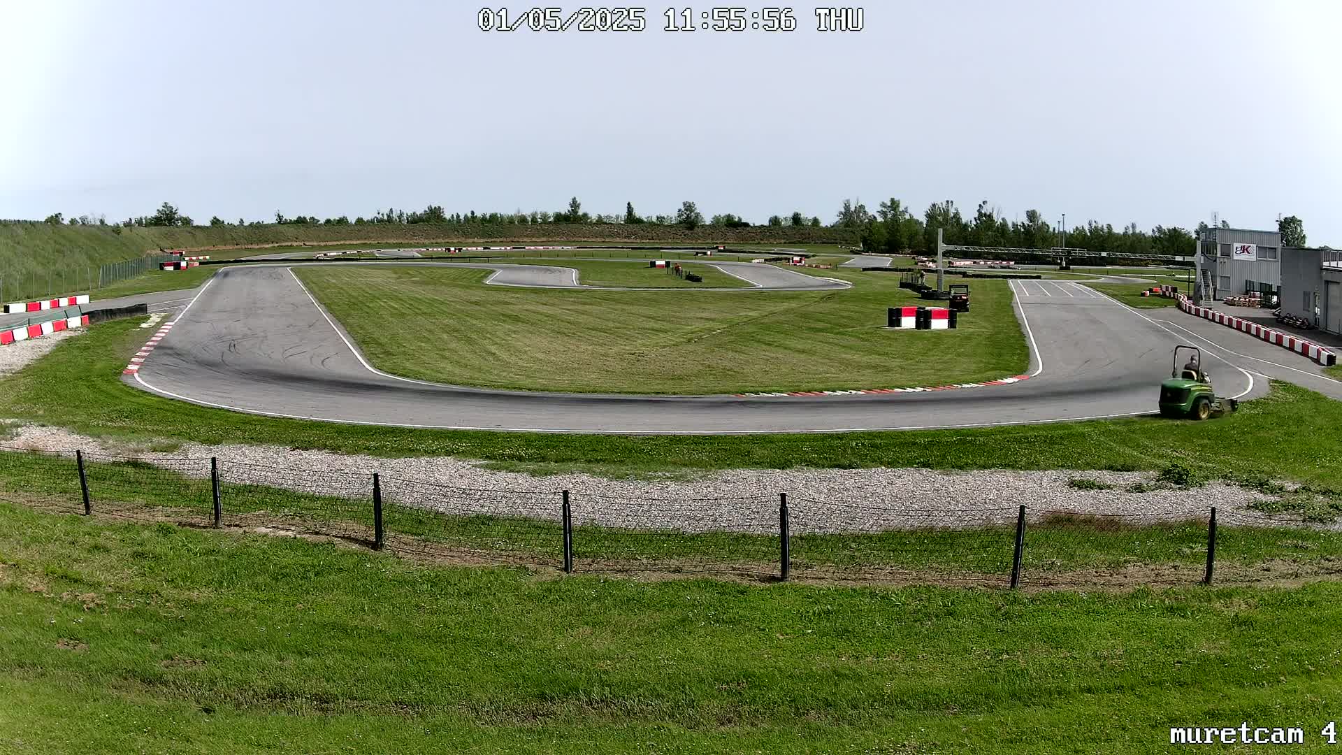 An outdoor go-kart track with a paved course and grassy areas is visible under a mostly clear sky.