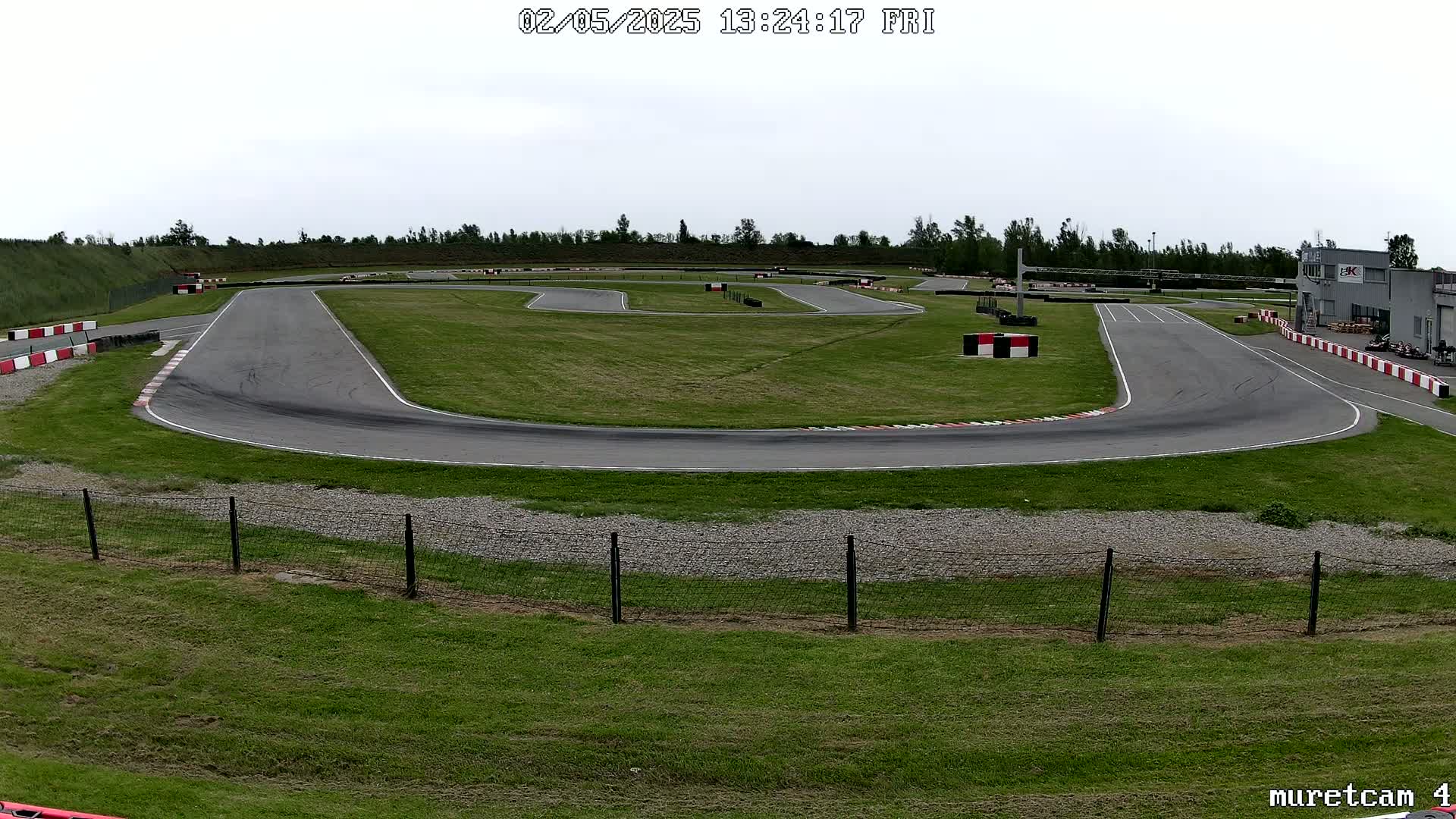 An outdoor go-kart track on an overcast day, with a paved course winding through a grassy area, bordered by fencing.