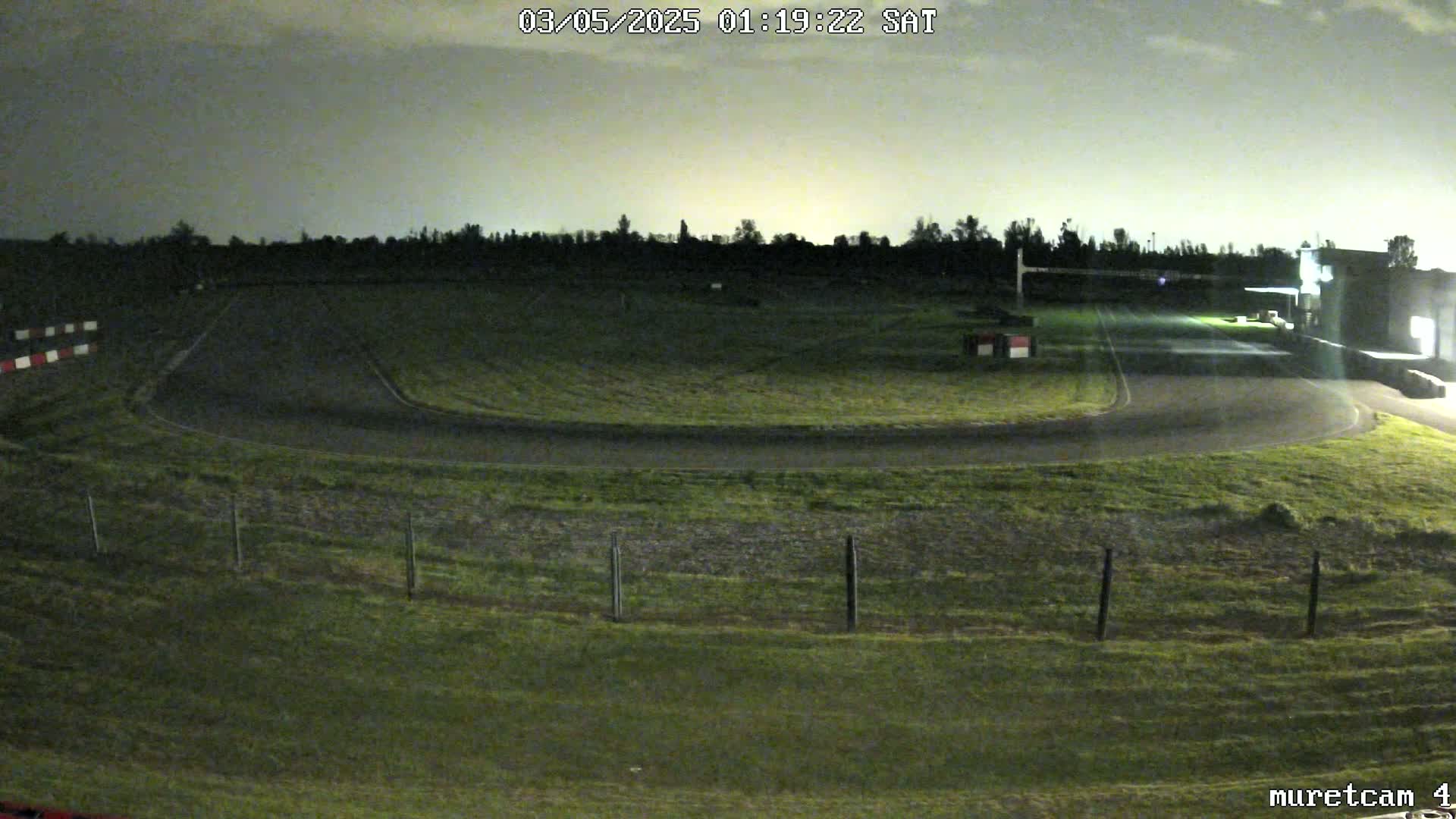 A nighttime view of a dimly lit race track, surrounded by grassy areas, under a cloudy sky.