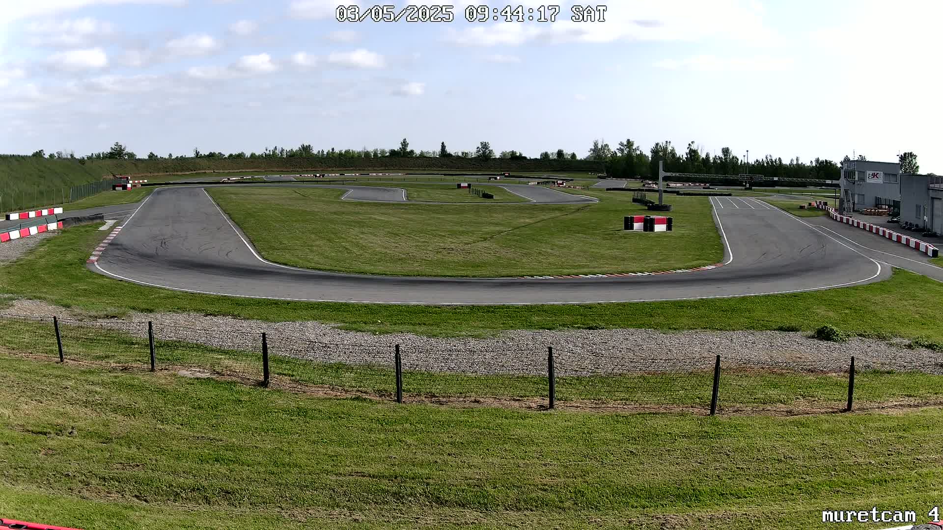 An outdoor go-kart track on a partly cloudy day with a building in the background.