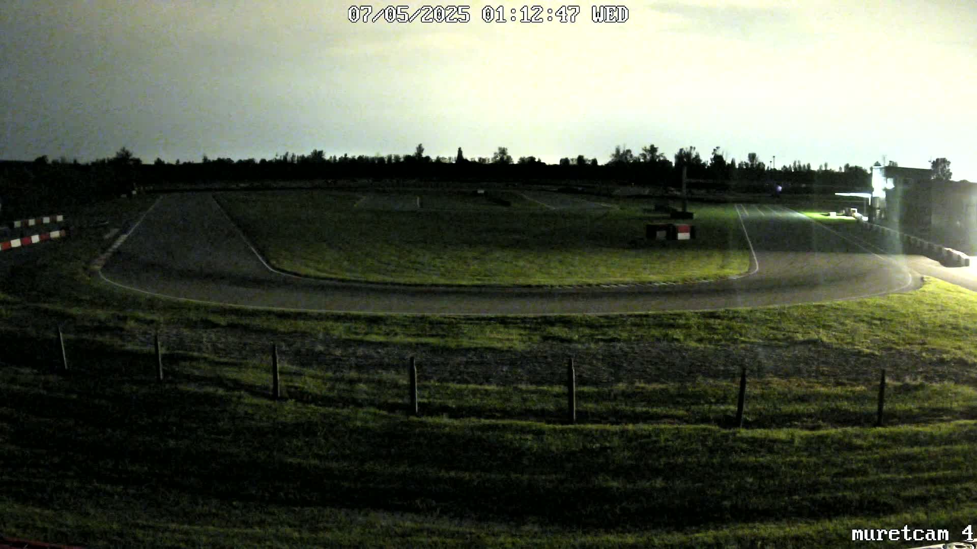 A dimly lit go-kart track at night under a cloudy sky.