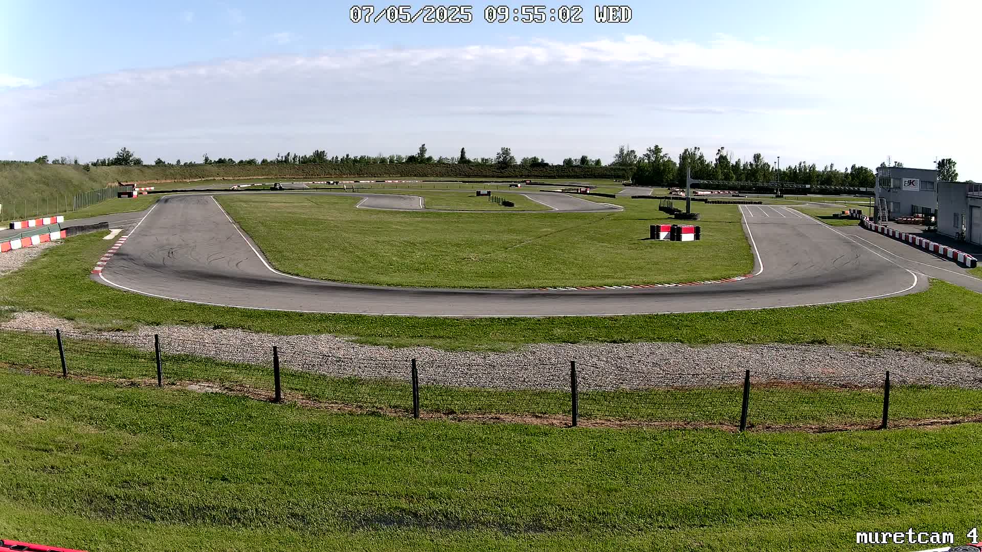 An empty asphalt go-kart track with green grass surrounds and a partly cloudy sky above.