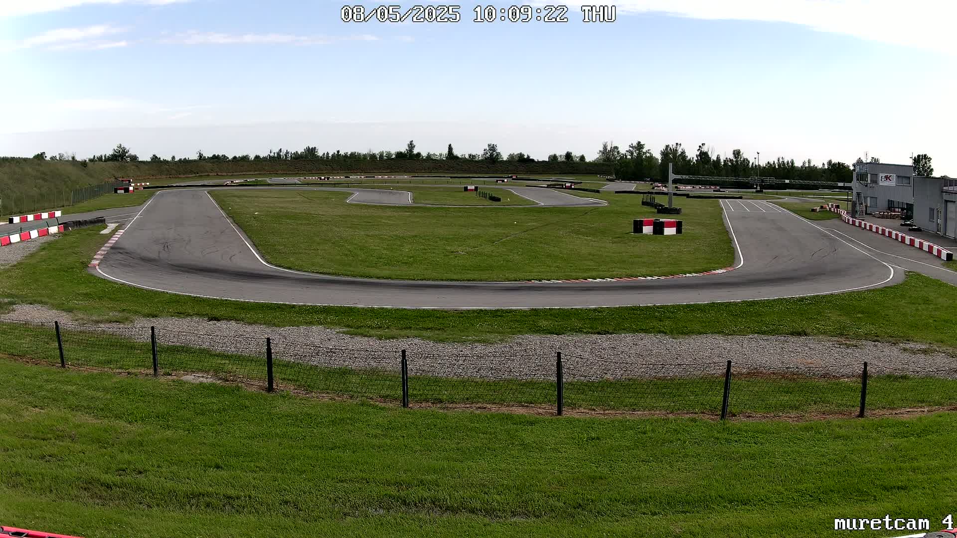 An outdoor go-kart track with a paved racing surface, surrounded by grassy areas and under a mostly clear sky.
