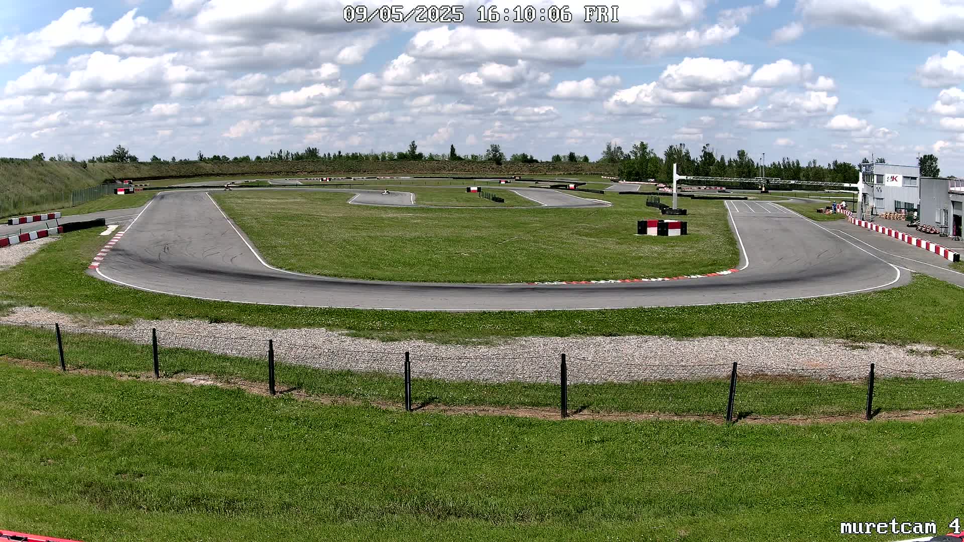 A go-kart track with a few go-karts visible on a partly cloudy day.