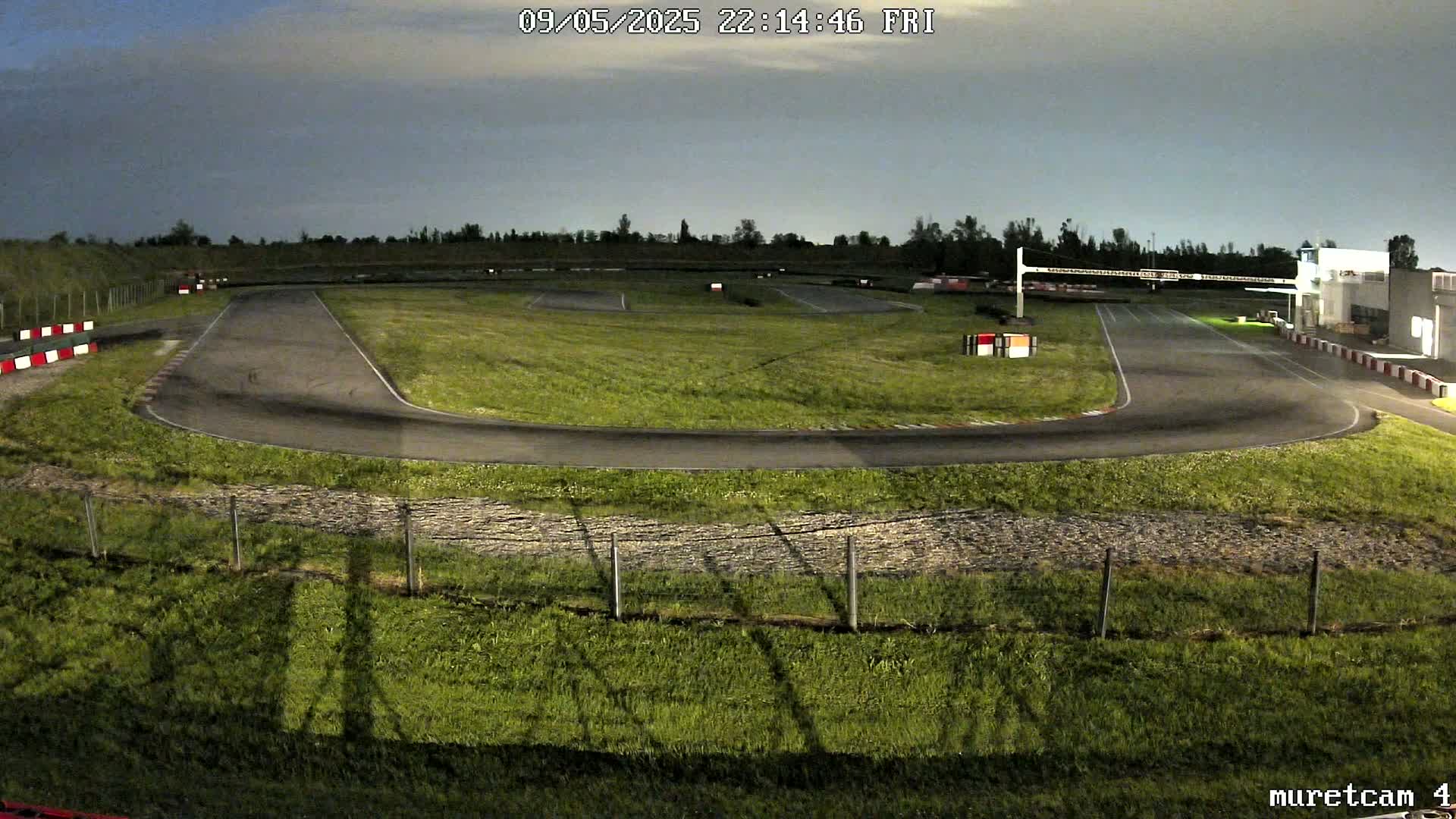 An empty asphalt go-kart track curves through a grassy area under a twilight sky.
