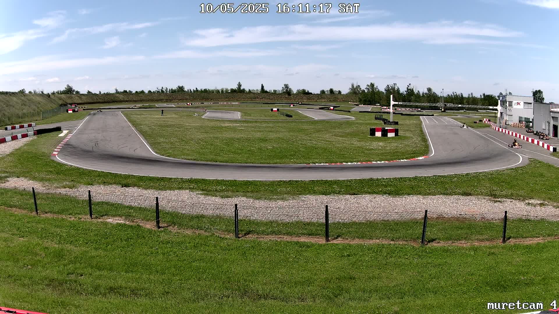 An outdoor go-kart track on a sunny day with several karts visible on the course.