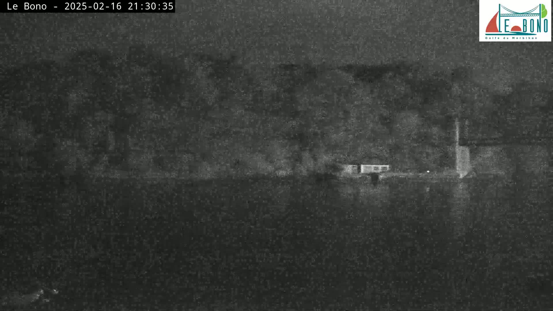 A nighttime, low-light image shows a dark body of water in front of a dark shoreline with some indistinct structures.