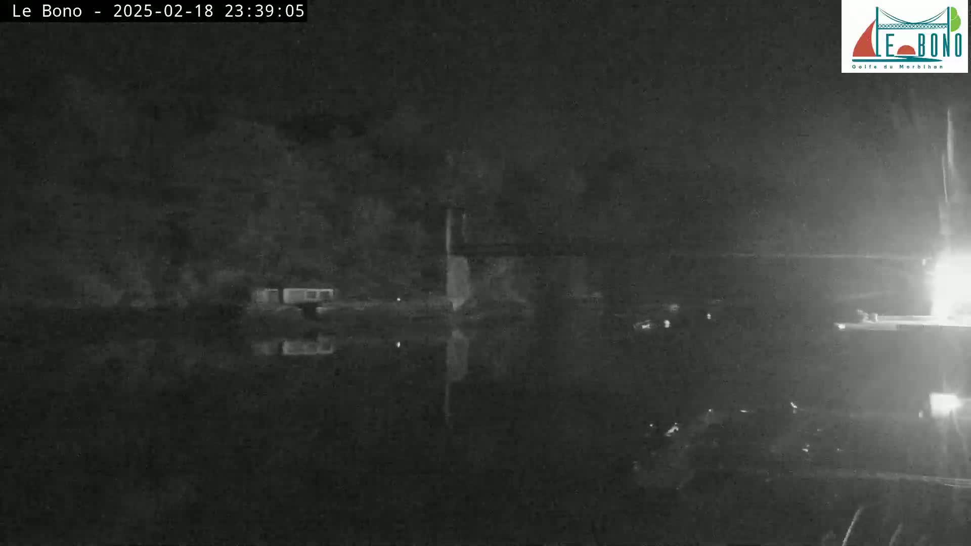 A nighttime, low-light image shows a dark body of water reflecting a dimly lit shoreline with sparse structures.