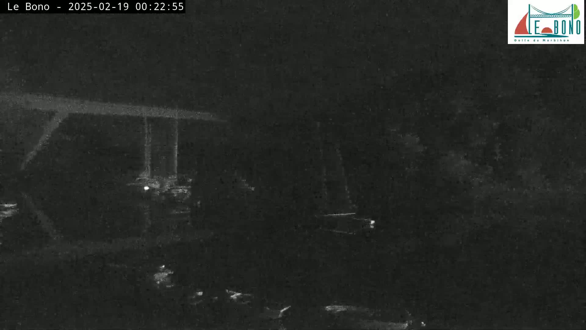 A low-light nighttime image shows a dark, shadowy outdoor scene with indistinct objects and a structure in the background.