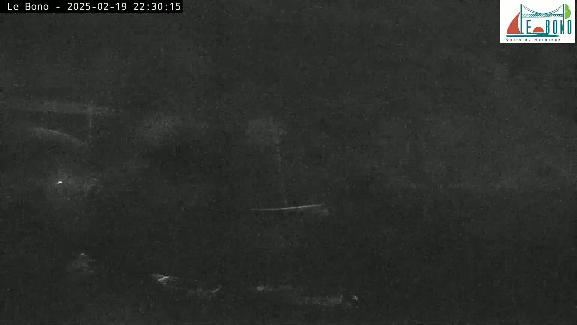 A nighttime, low-light image shows a dark, mostly featureless scene with a few faint light sources visible in the distance.
