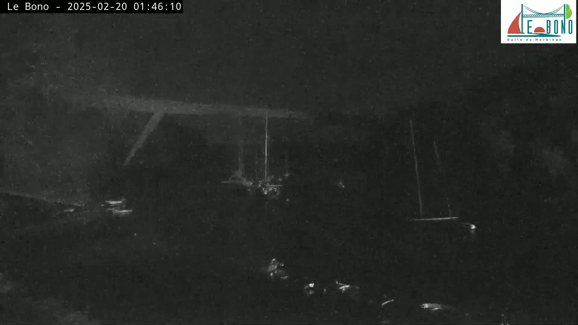 A low-light nighttime image shows a dark, indistinct scene with faint, blurry lights in the distance.