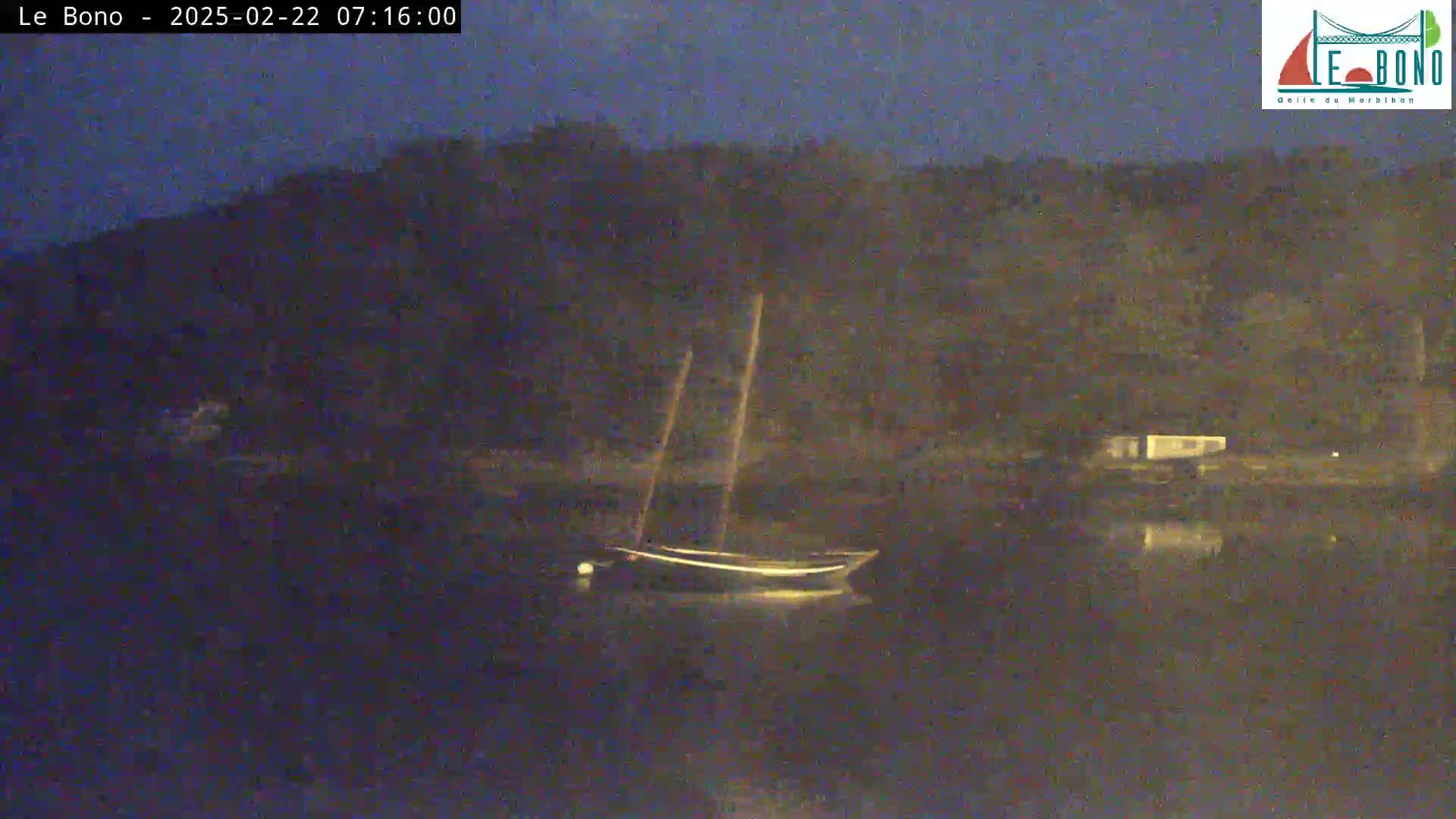 A sailboat is moored in dark, calm water at night, with a dark shoreline in the background.