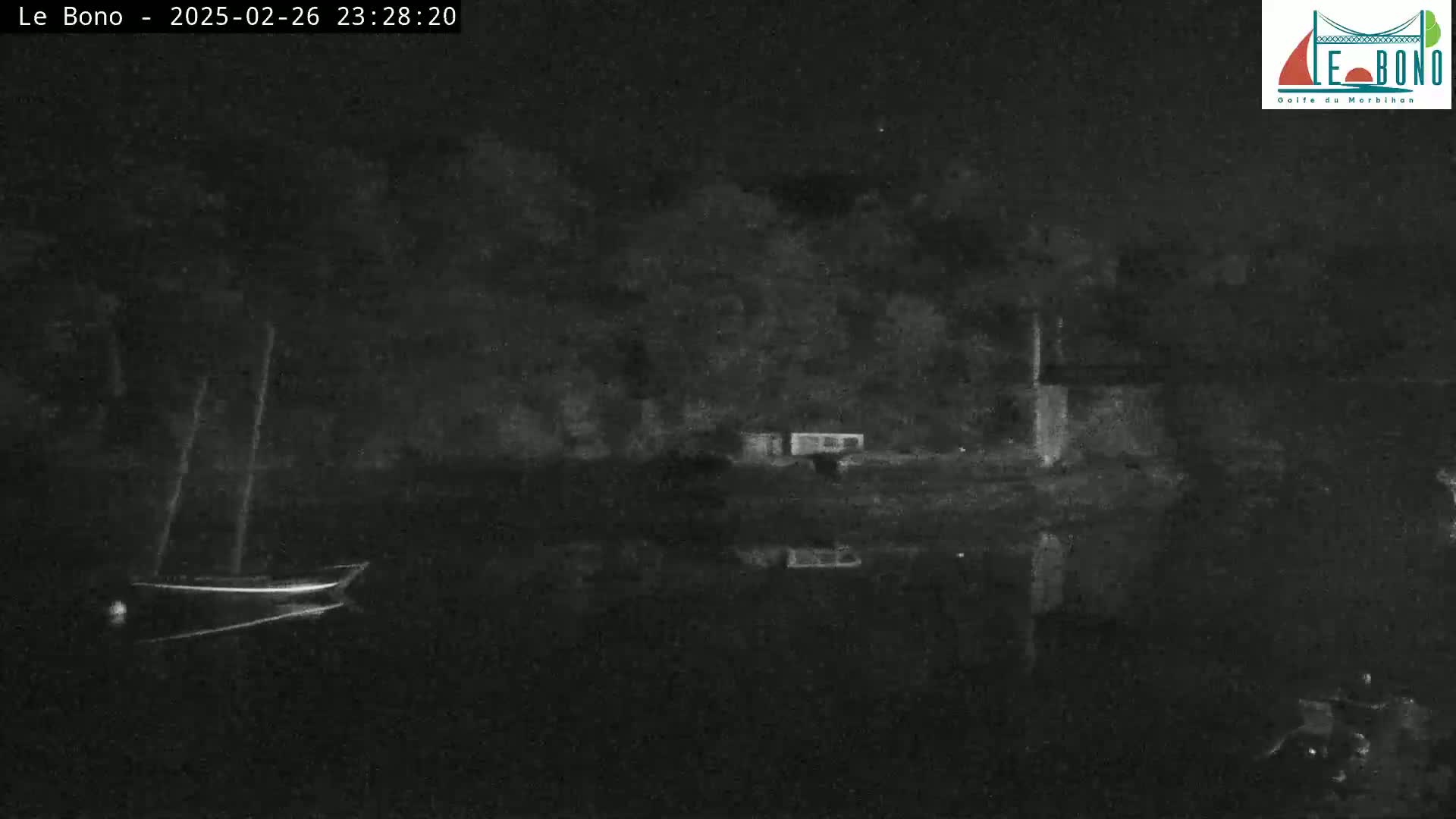 A small sailboat is moored near the shore of a dark body of water at night, under a clear sky.