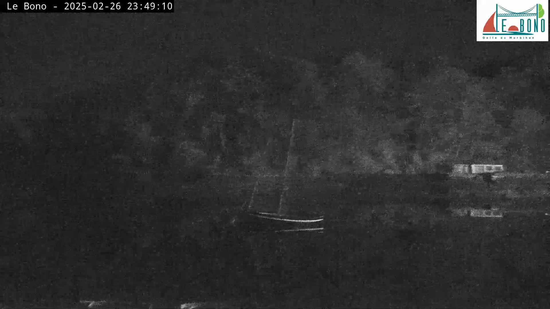 A small sailboat is moored near a dark shoreline at night under a cloudy sky.