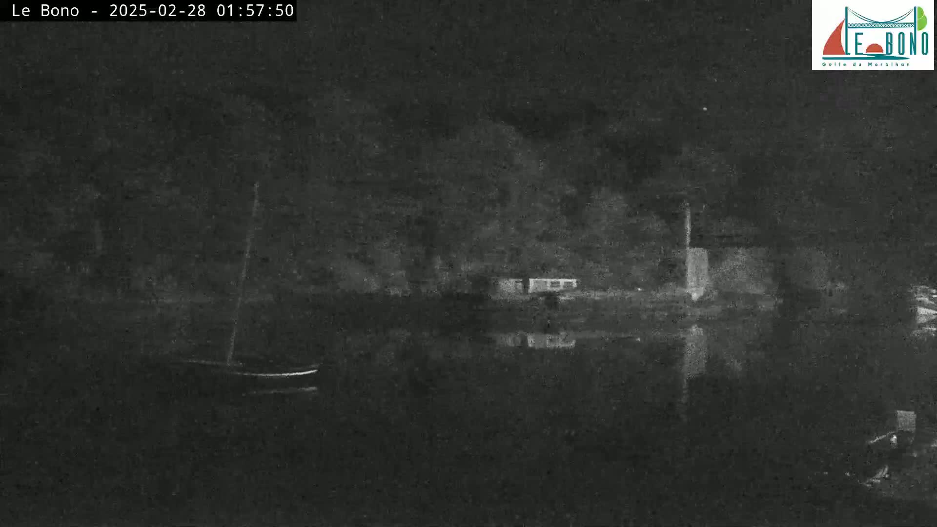 At night, a body of dark water reflects the shadowy outlines of trees and a small boat at a dock.