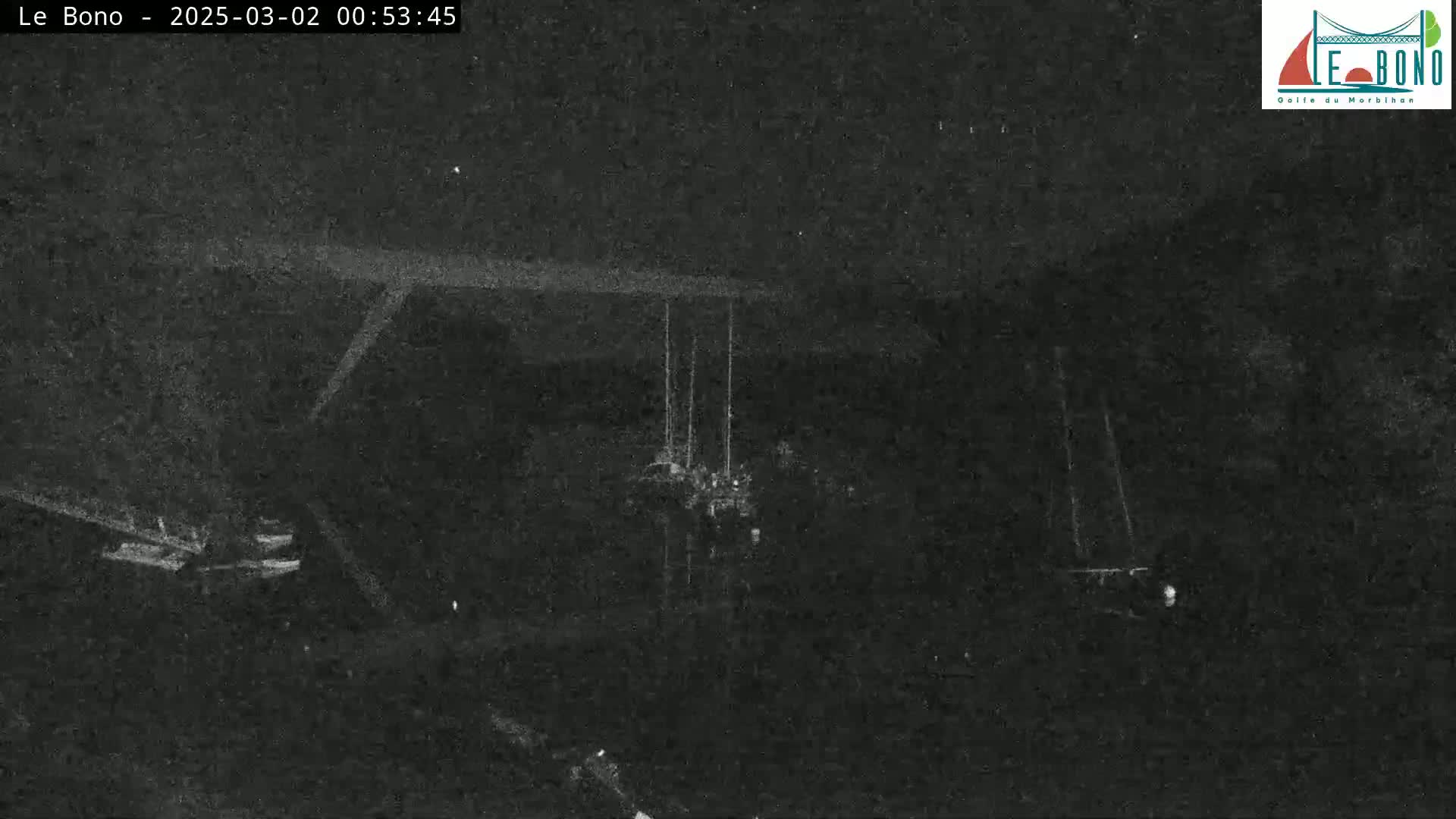 A low-light, nighttime image shows a dark scene with faintly visible structures and what appears to be a tall, thin object in the center, possibly under a structure.