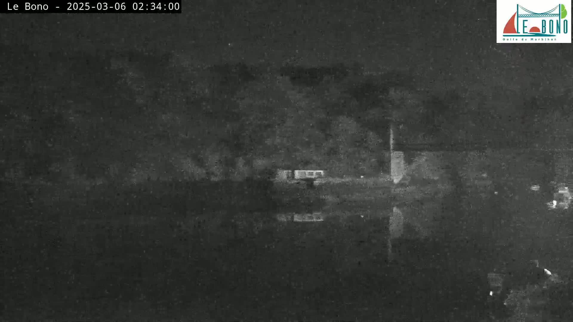 A nighttime, low-light image shows a dark body of water reflecting a dark shoreline with sparse, indistinct structures.