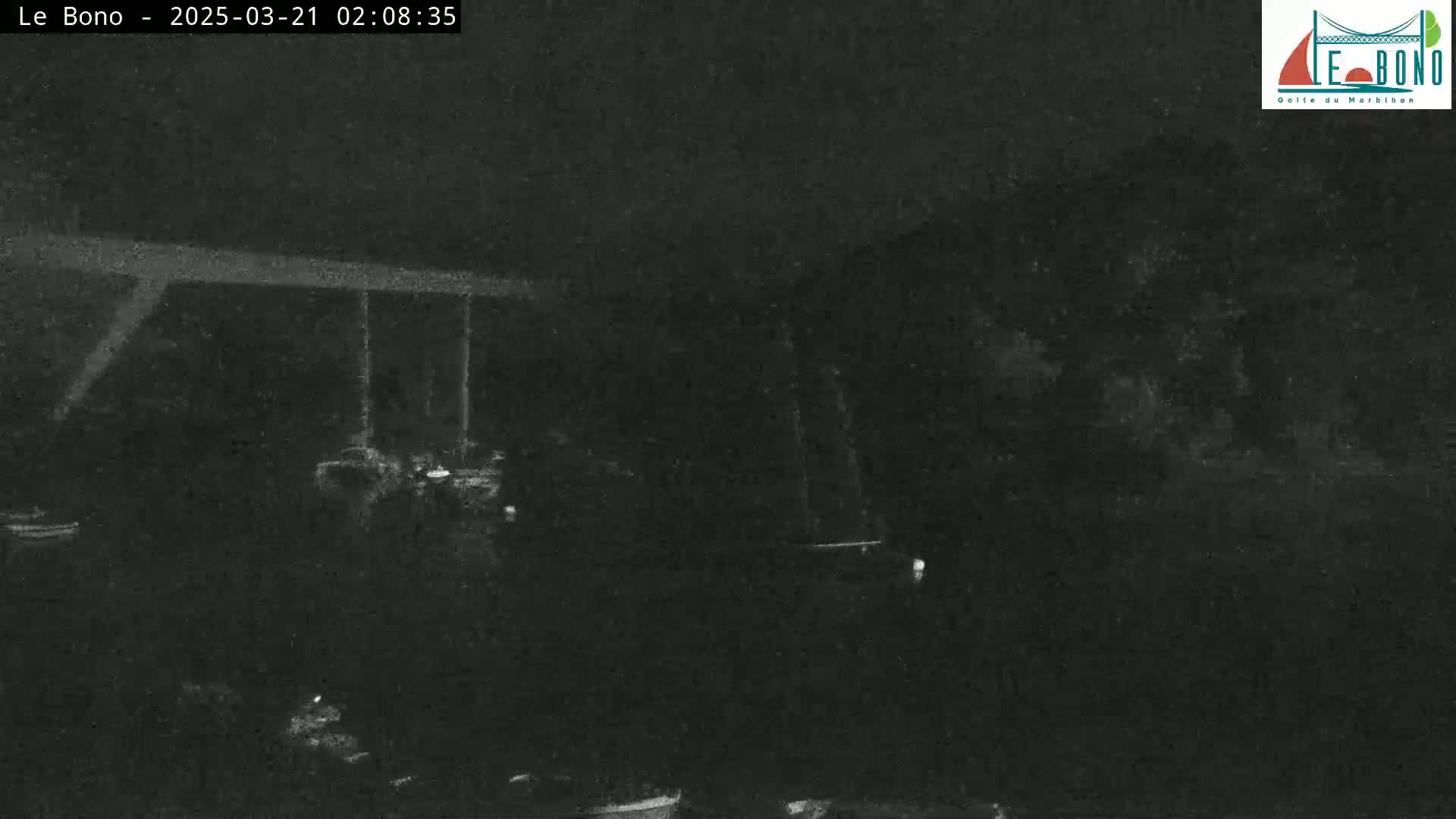 A nighttime, low-light image shows a dark, indistinct outdoor scene with some structures and possibly vehicles barely visible.
