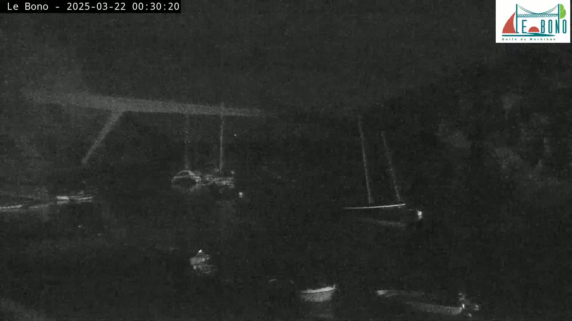 A nighttime, low-light image shows a dark, possibly water-bound area with indistinct shapes suggestive of boats or vehicles.