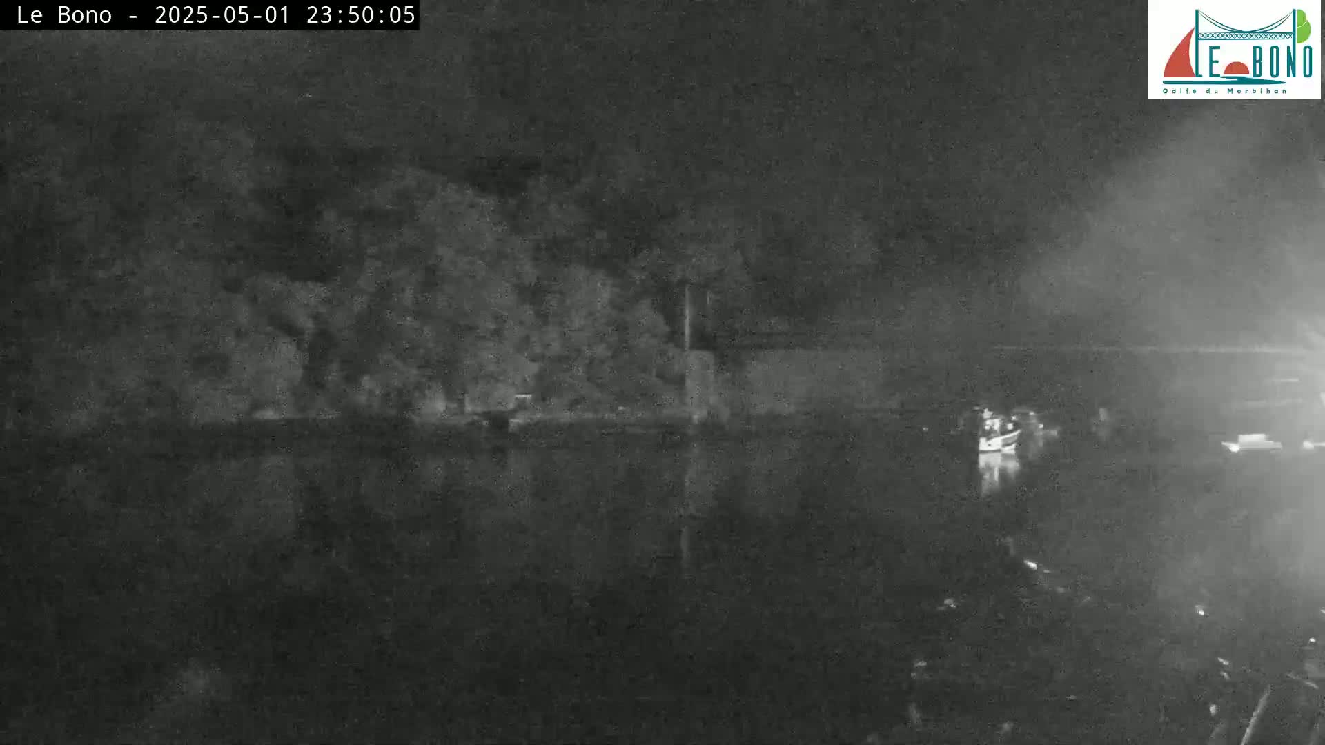 A nighttime, low-light image shows a dark body of water reflecting a dark shoreline with trees.