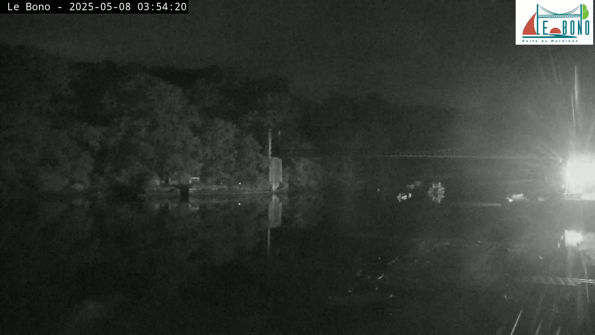 A nighttime view of a dark body of water reflecting the trees and structures on its bank under a clear, dark sky.