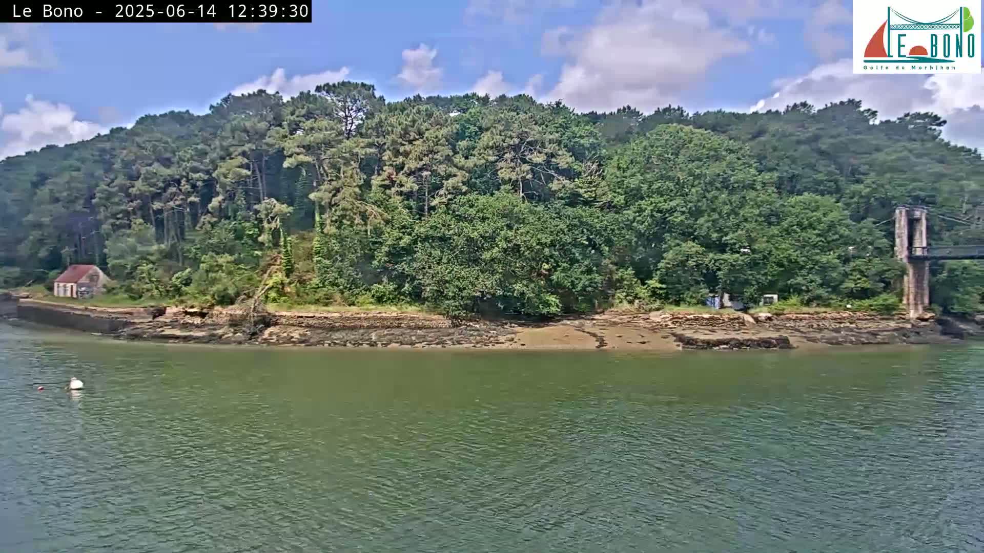 A small, rocky shoreline with a lone house and lush green trees under a partly cloudy sky, is visible across a calm body of water.