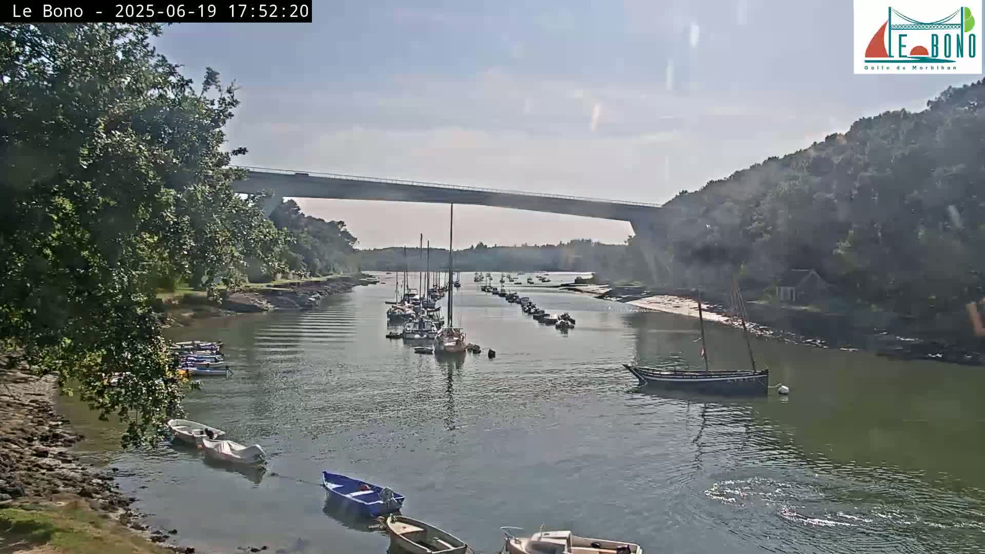 Numerous boats are moored in a calm waterway under a bridge on a sunny day.
