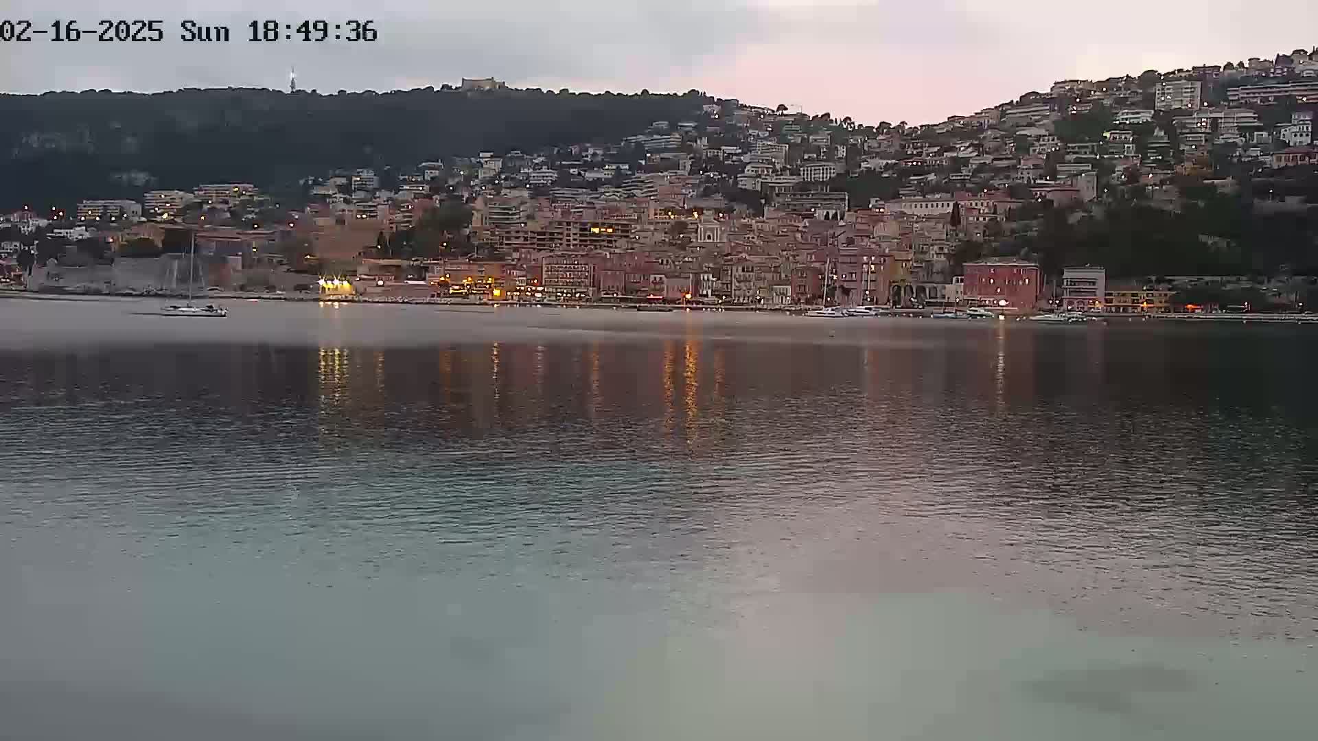 A town on a hill overlooking a calm body of water at dusk.