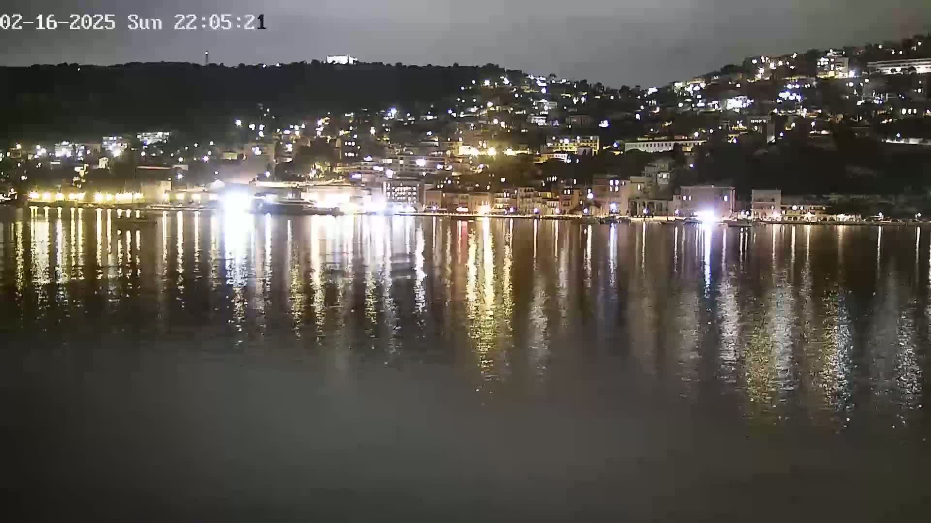 A nighttime view of a city's waterfront, illuminated by lights reflecting on calm water.