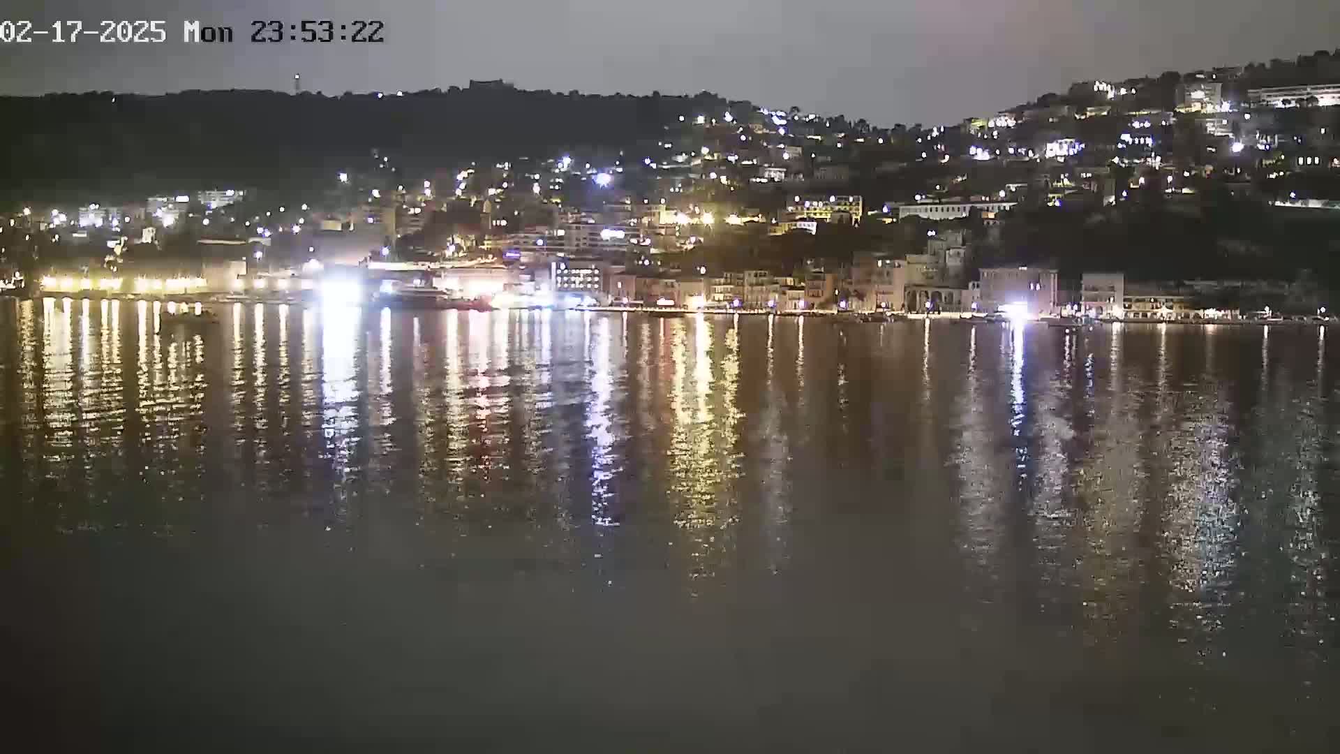 A nighttime view of a town's waterfront, illuminated by many lights reflected in calm water.