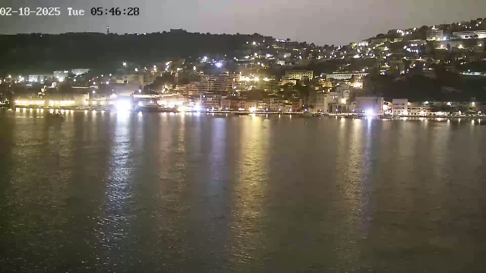 A nighttime view of a city's waterfront, illuminated with lights reflecting on calm water.