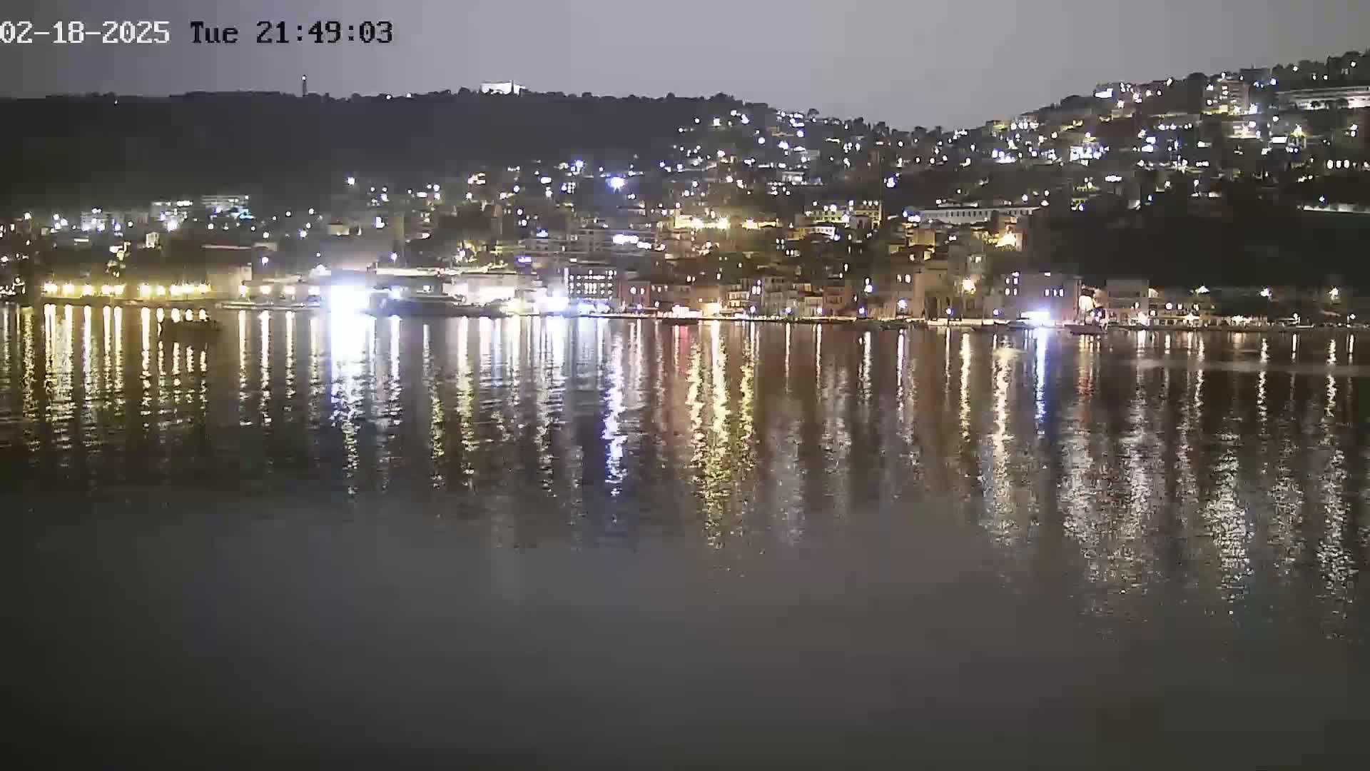A nighttime view of a waterfront town with its lights reflected on a calm body of water.