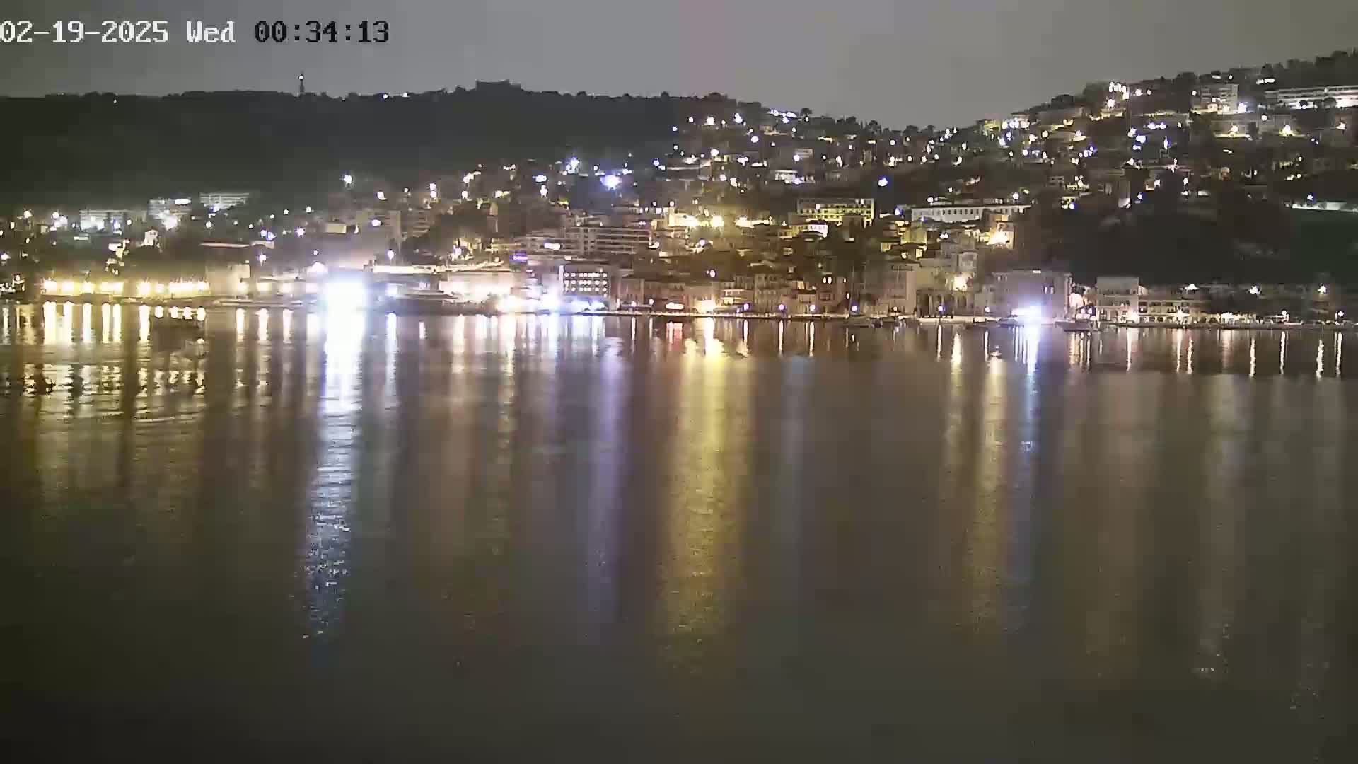 A nighttime view of a city's waterfront, illuminated by lights reflecting on calm water.