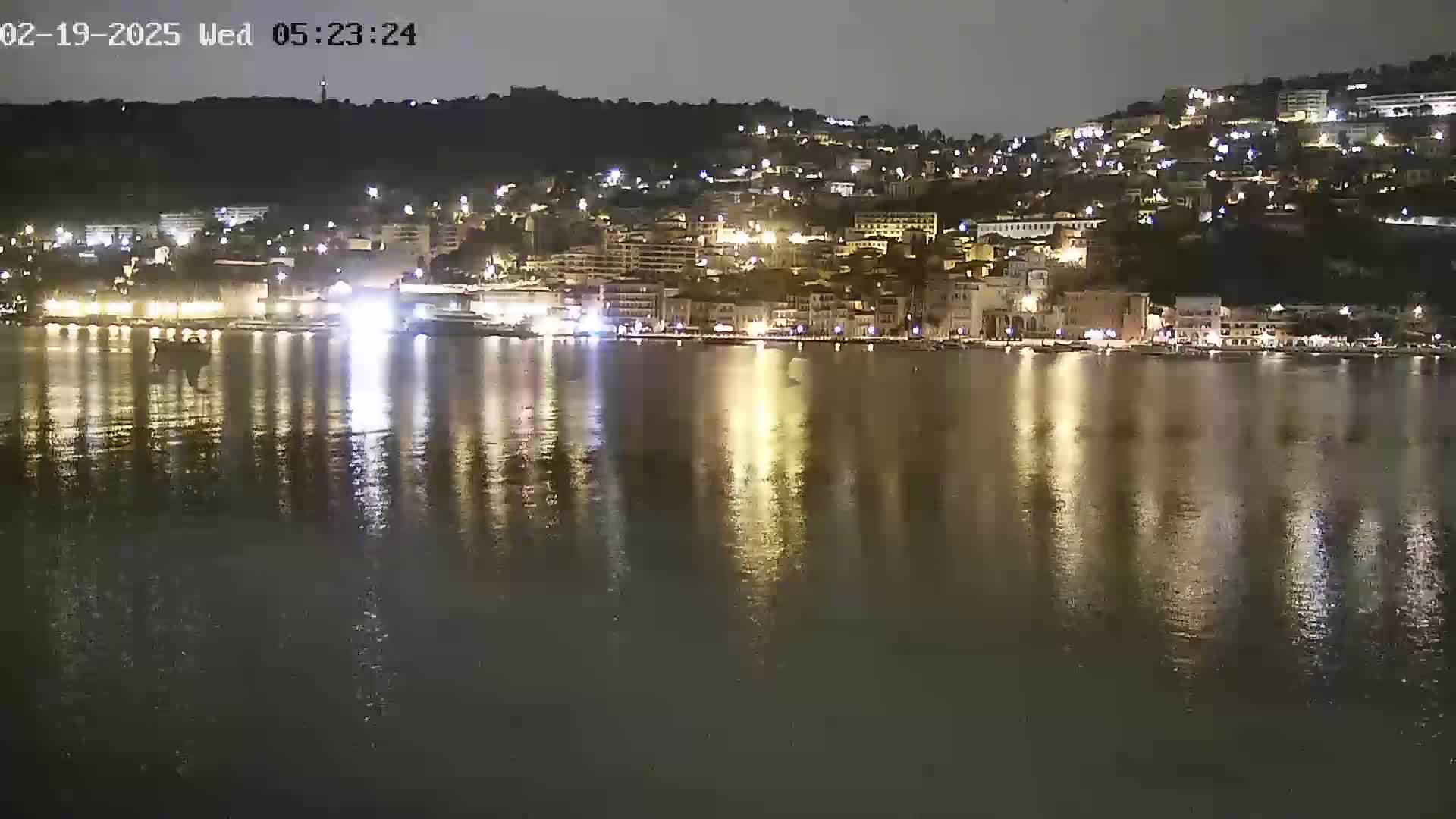 A nighttime view of a waterfront town illuminated with lights reflected on calm water.