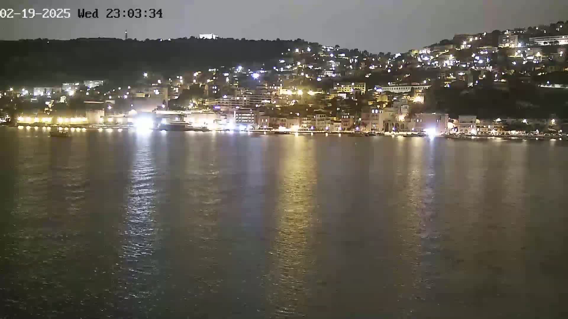 A nighttime view of a city's waterfront, illuminated by lights reflecting on calm water.