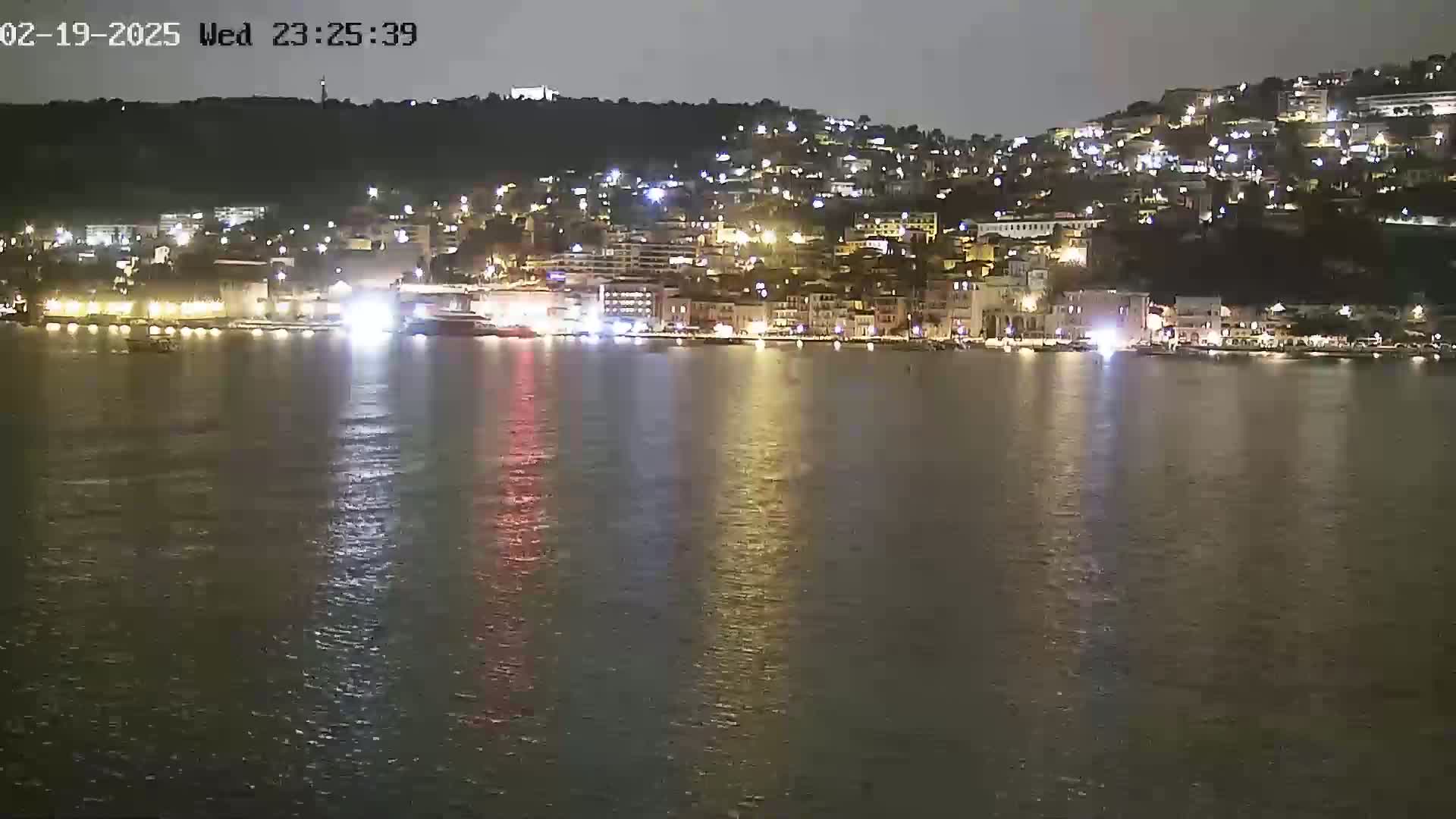 A nighttime view of a town's waterfront, illuminated by lights reflecting on calm water.