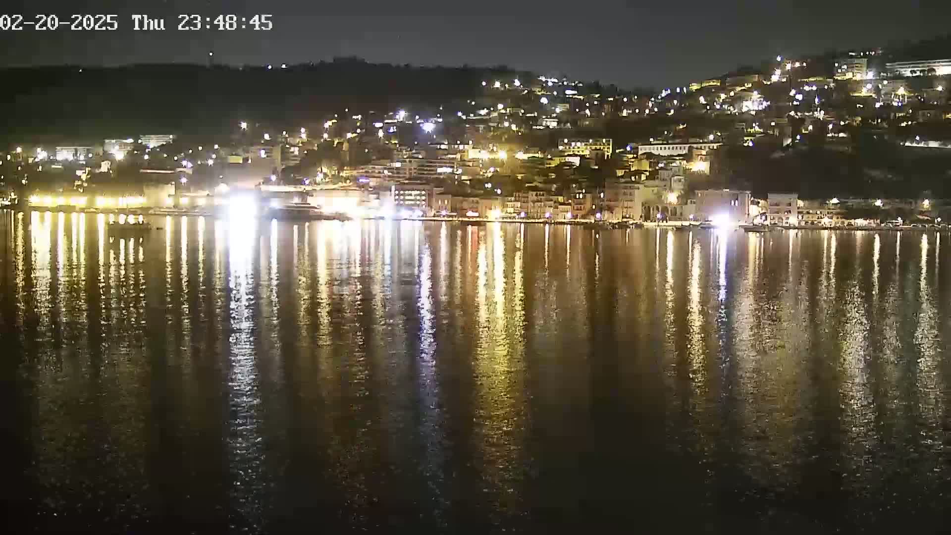 A nighttime view of a waterfront town, illuminated by lights reflecting on calm water.