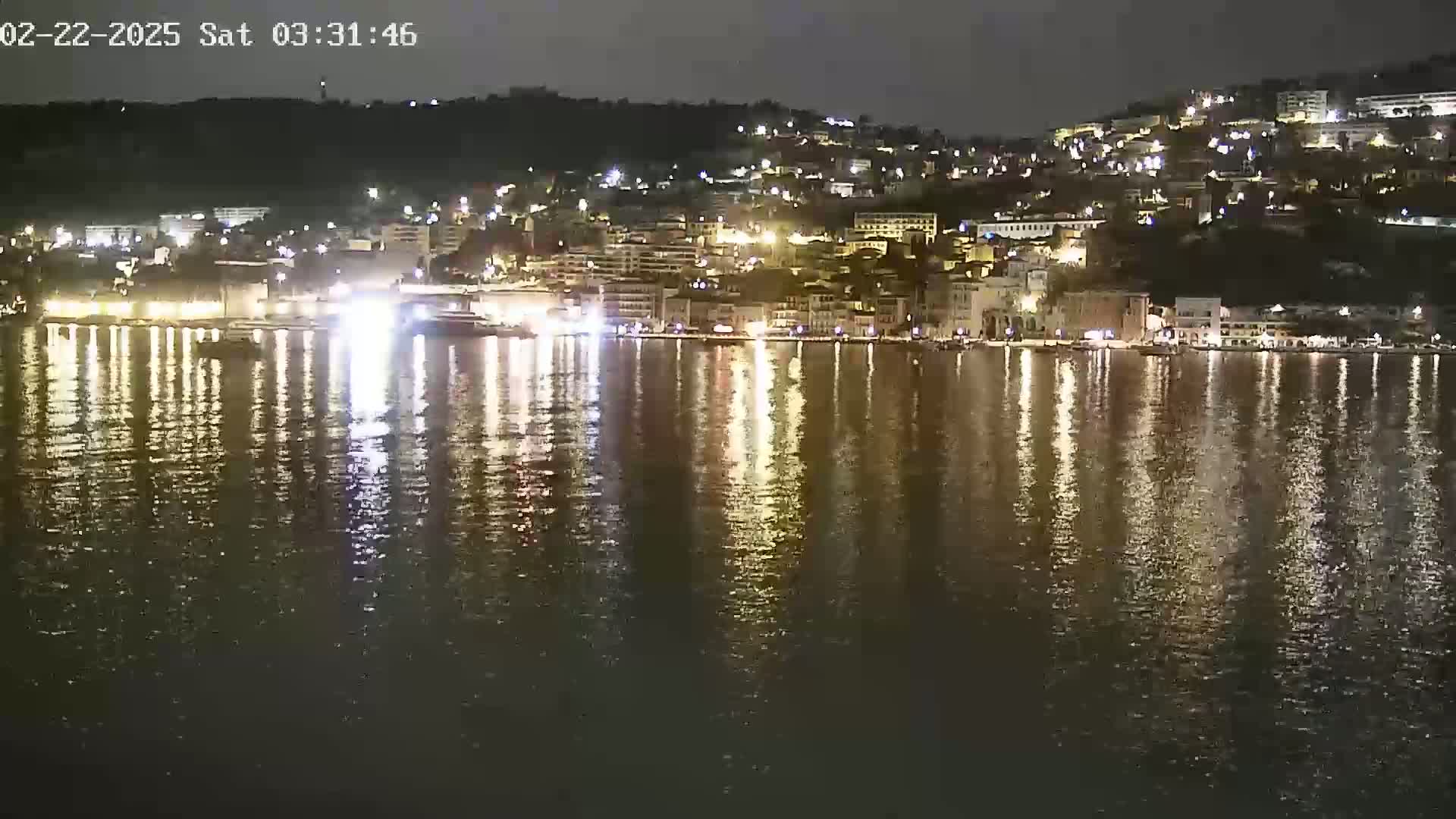 A nighttime view of a city's waterfront, illuminated by lights reflecting on calm water.