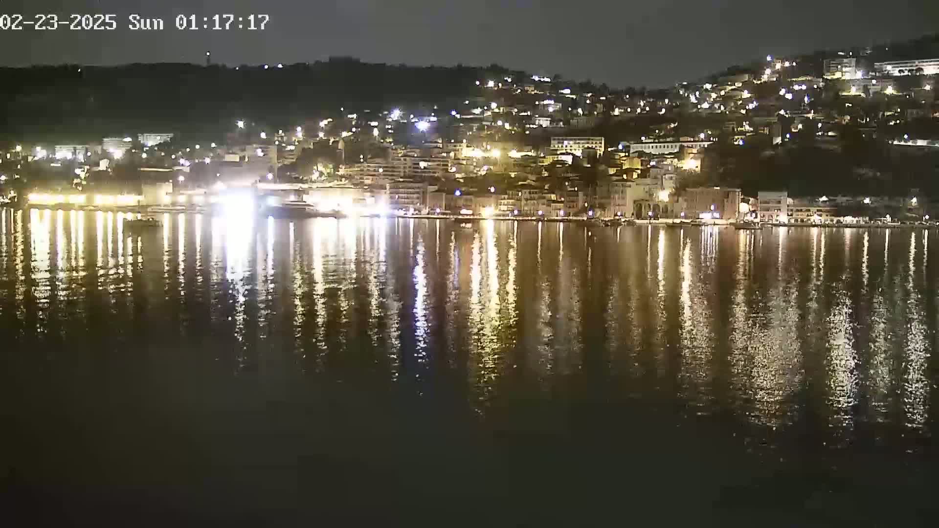 A nighttime view of a town's waterfront, brightly lit buildings reflected in calm water.