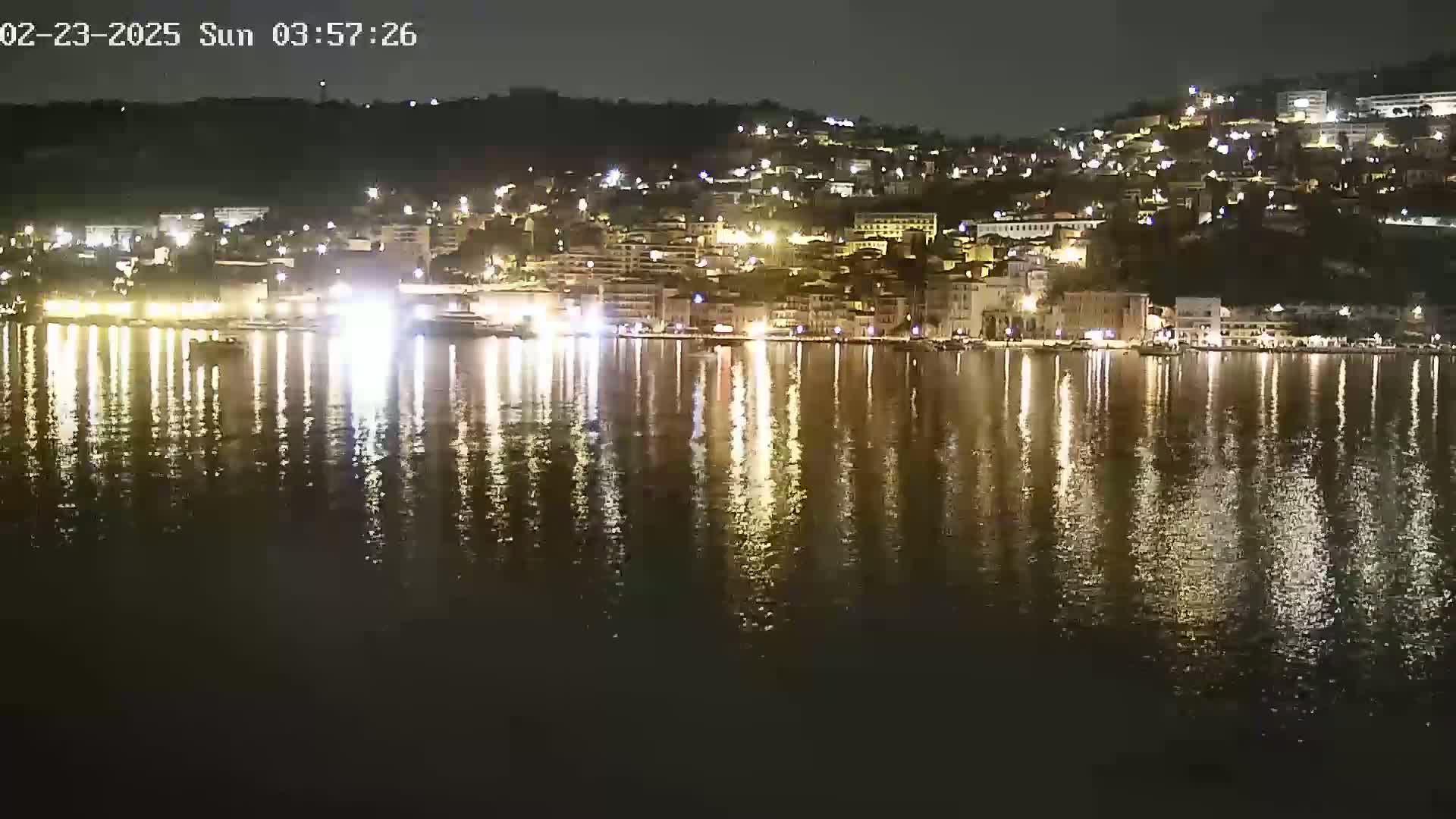A nighttime view of a waterfront town with many lights reflected in a calm body of water.
